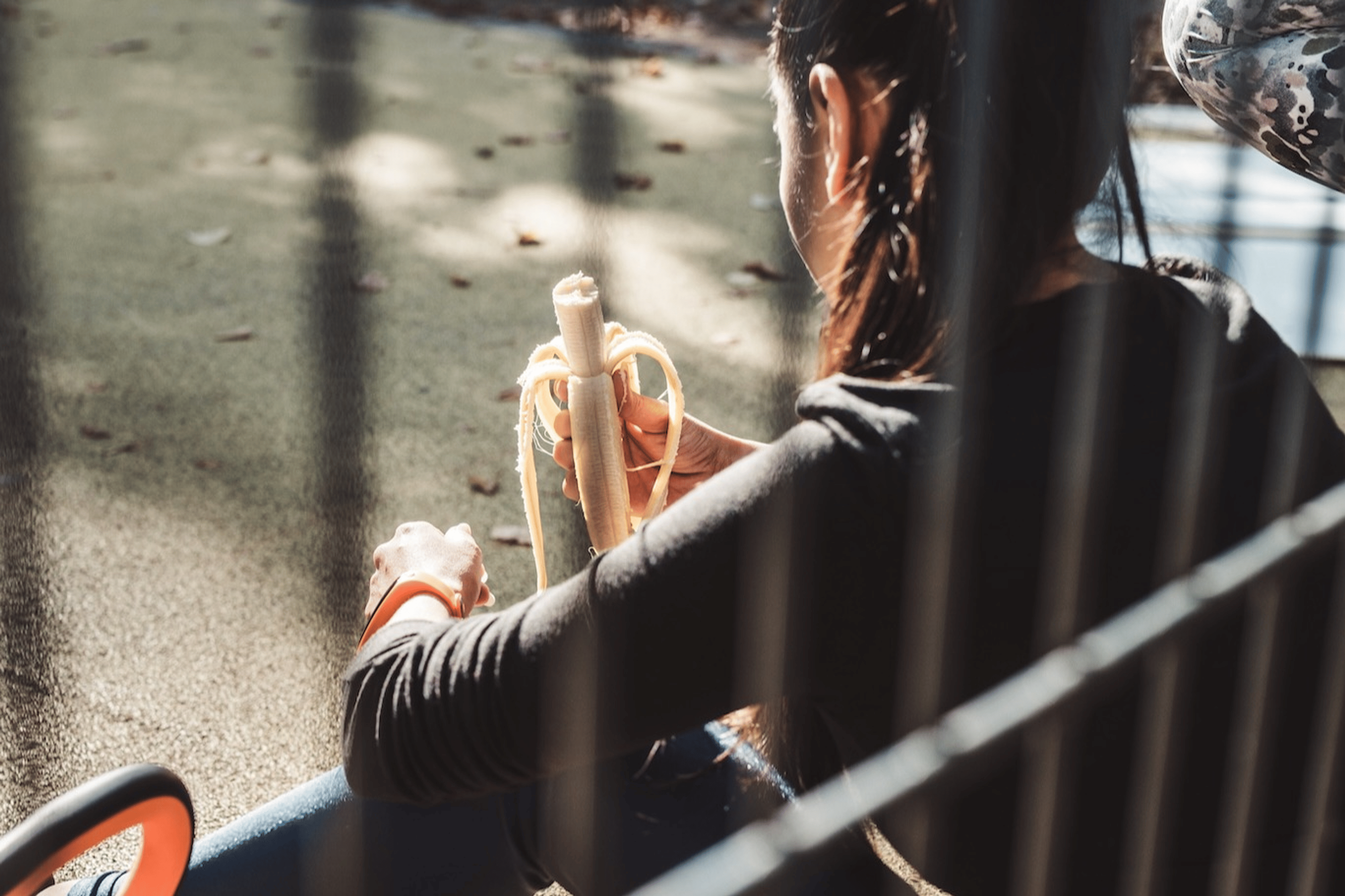 A back view of a runner sitting outside on a step and eating a banana. Bananas are great high-carb foods for runners.