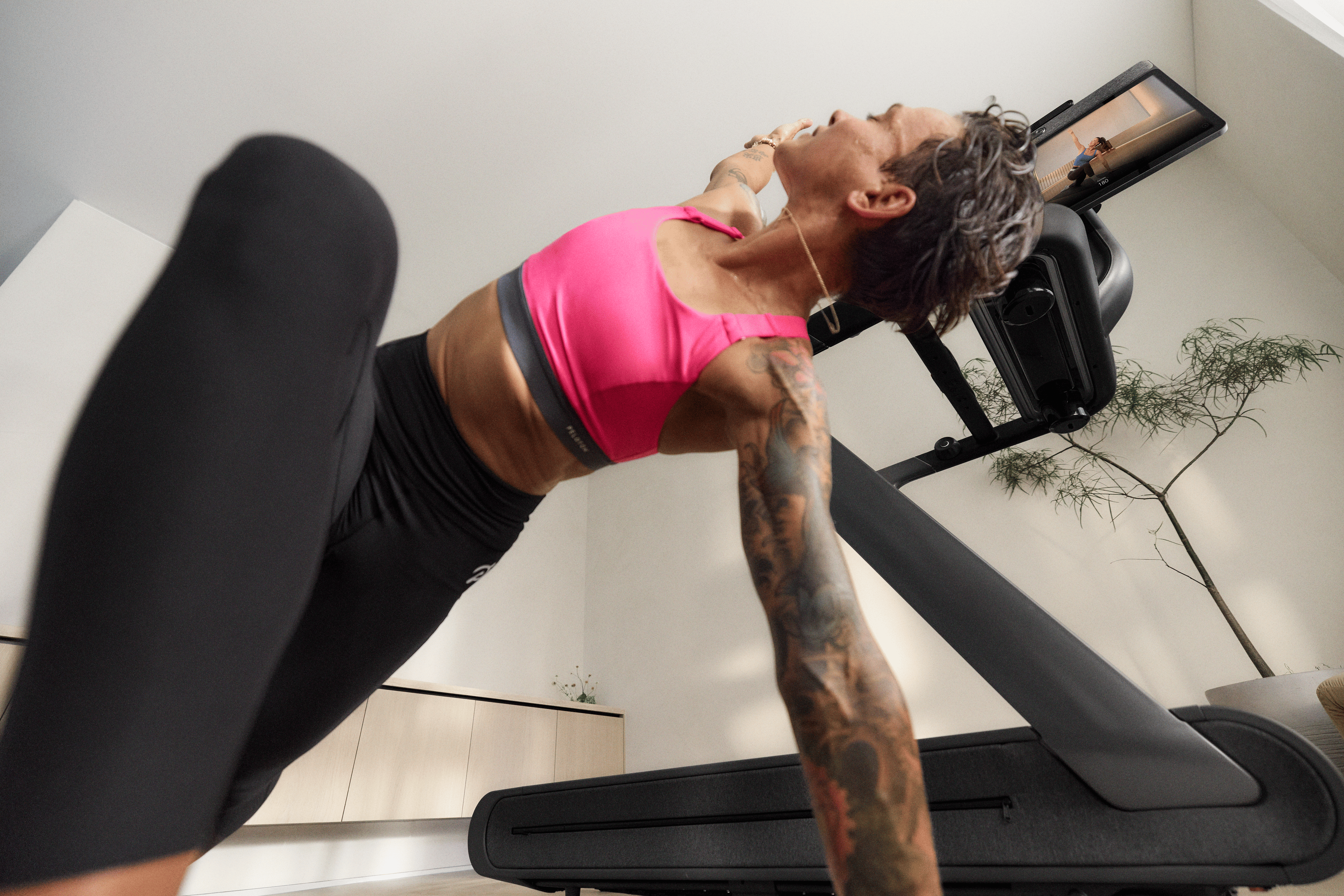 Woman stretching next to the Peloton Cross Training Tread+ as part of her cross training fitness routine. 