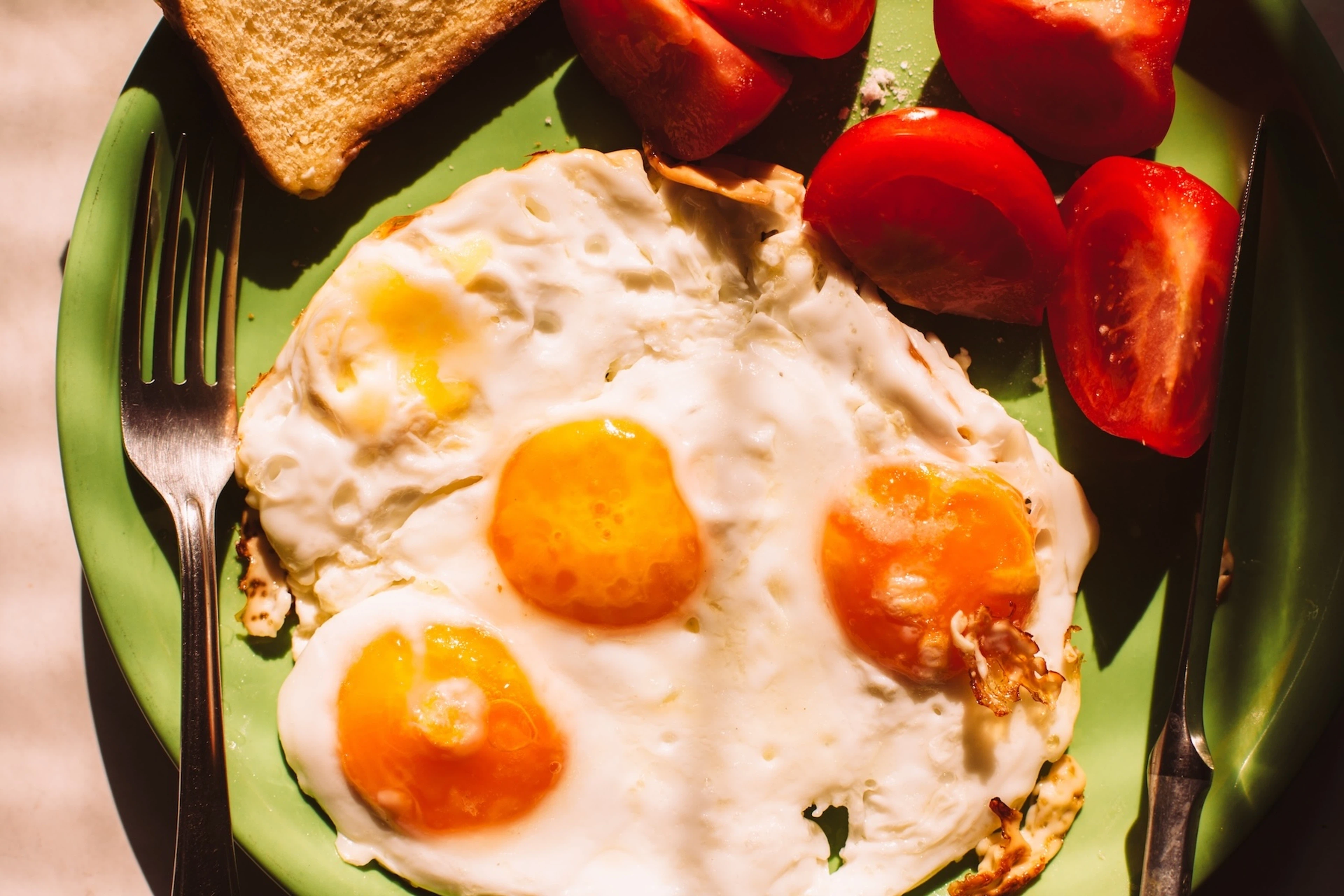 Three fried eggs on a plate with tomatoes and toast.