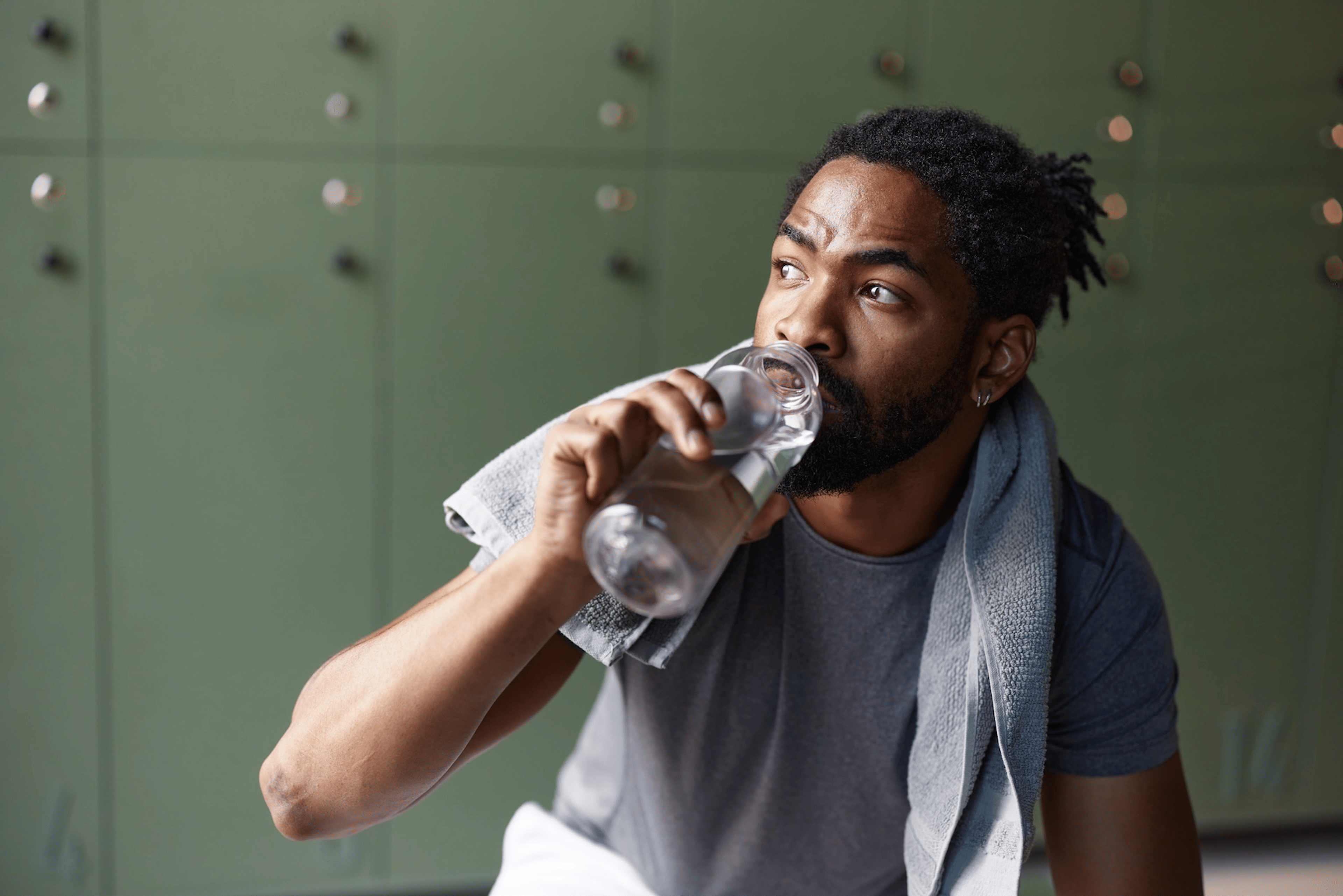 A man drinking water in a gym locker room. He is drinking water to gain muscle.