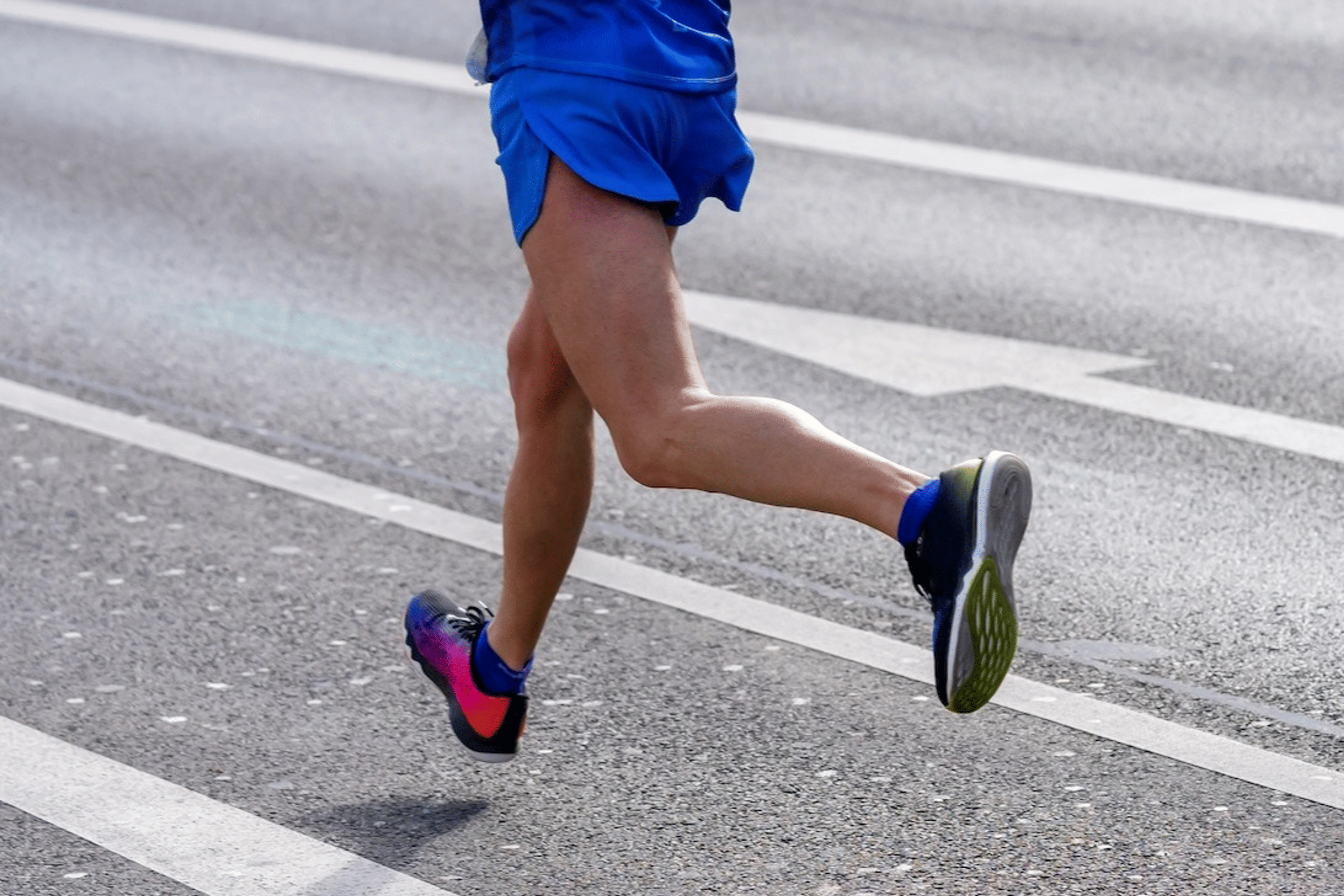 A close-up view of a runner's legs running on an outdoor paved road.
