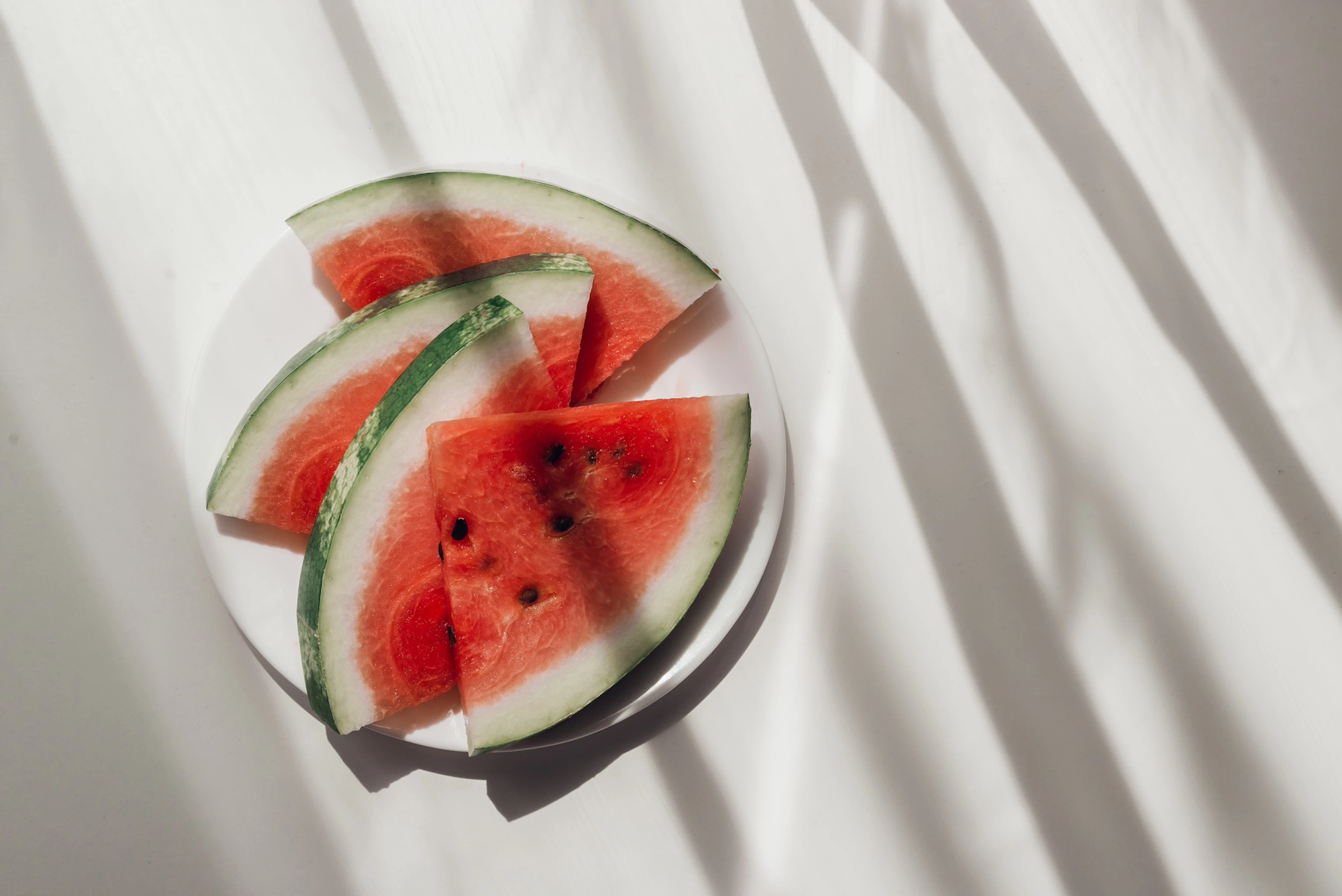 Slices of watermelon, a hydrating food, sitting on a white plate on top of a white table.