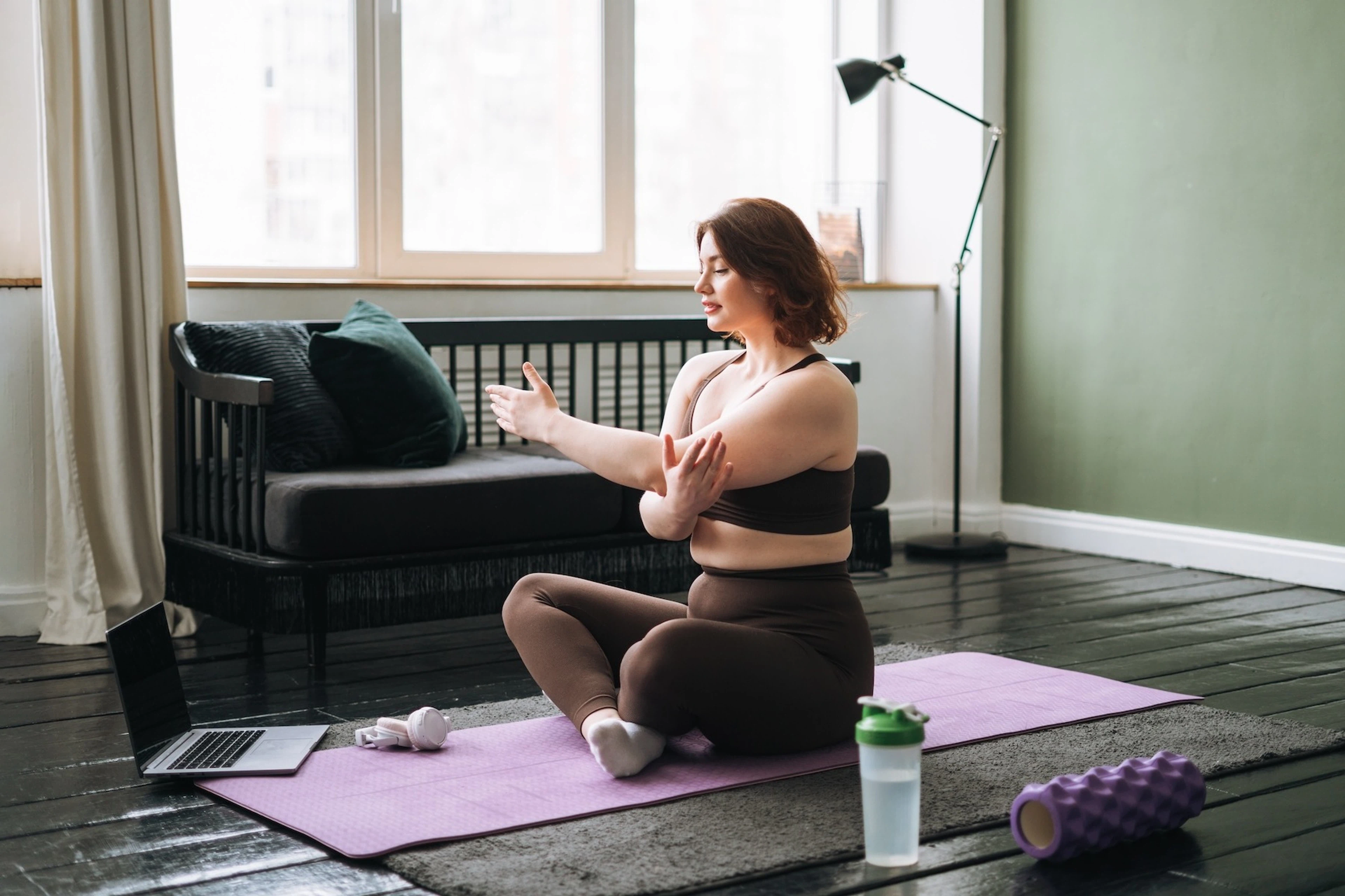 A woman sitting down on a yoga mat, stretching her arms on a rest day.