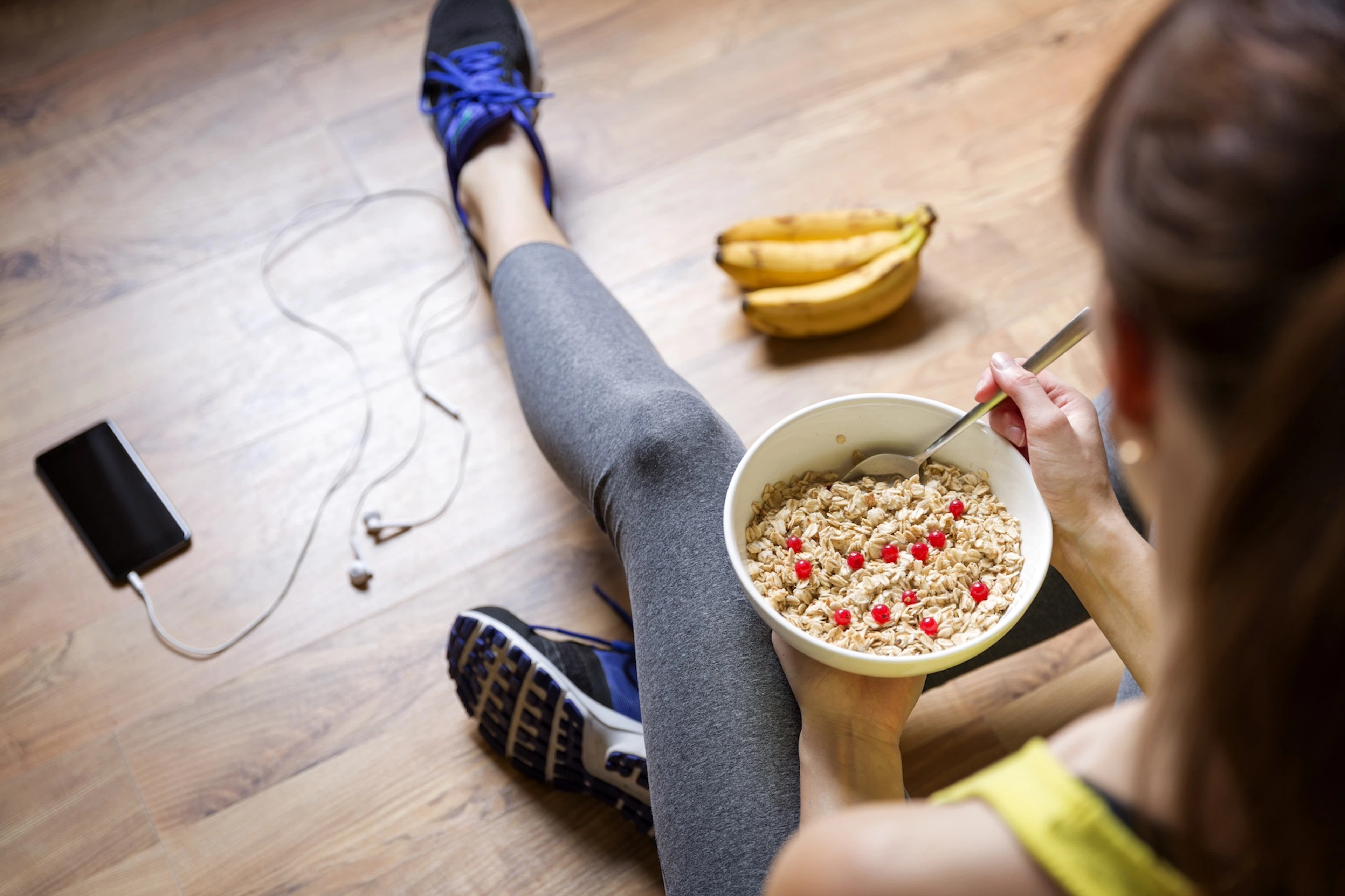 A woman eating oatmeal and a banana before going on a morning run. Her phone and headphones are on the floor next to her.