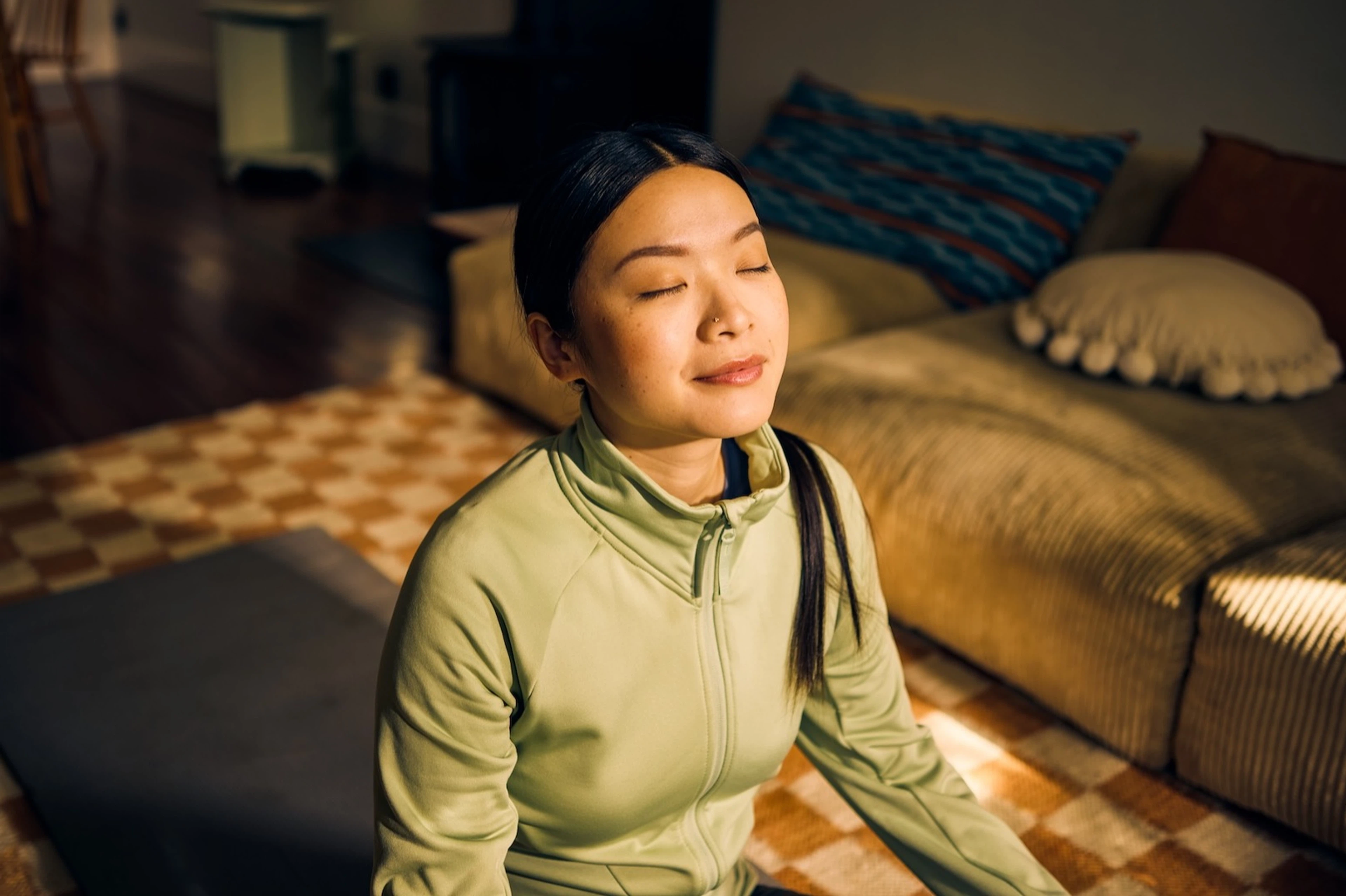 A woman practicing breathwork on a yoga mat in her living room.