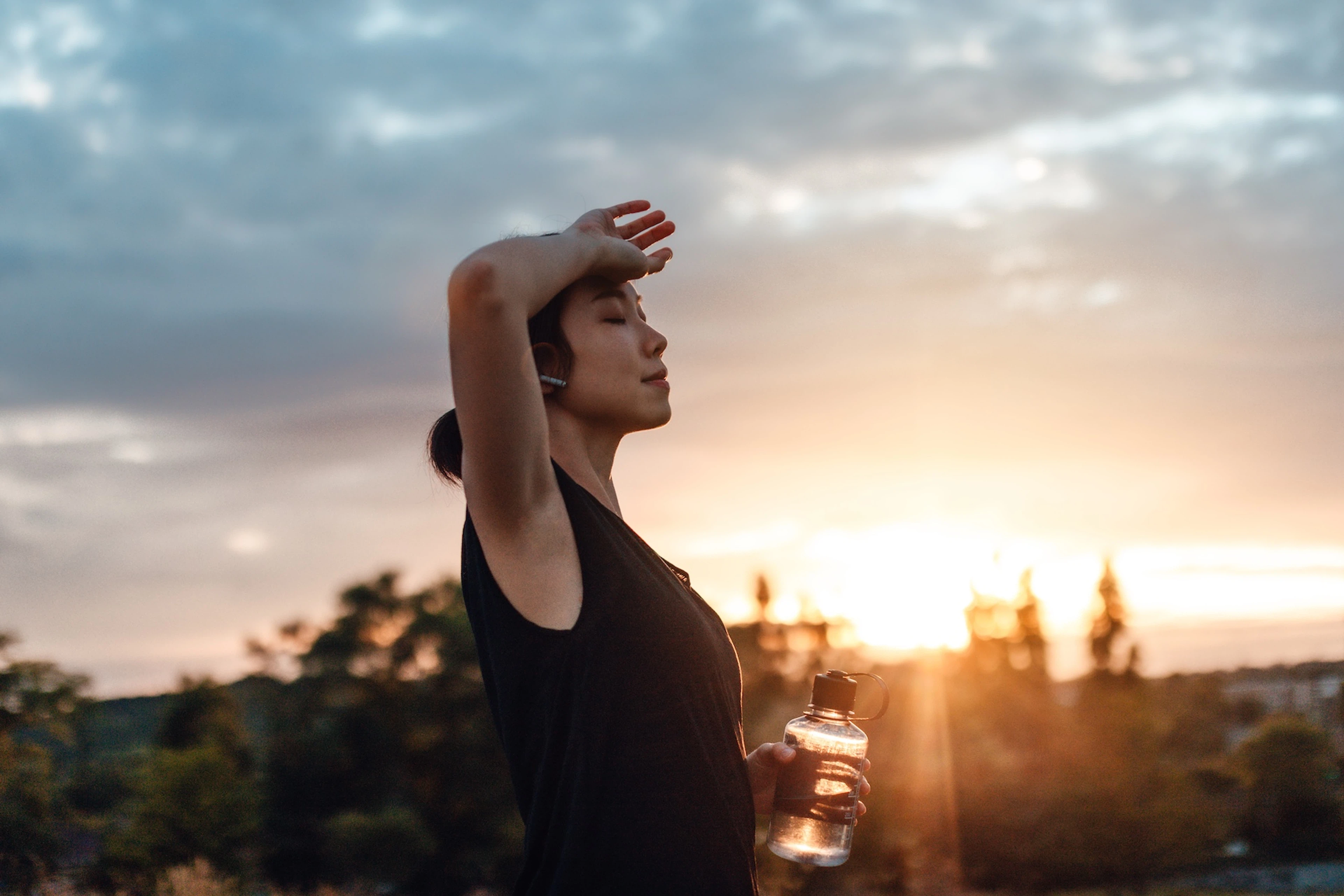 A woman closing her eyes with her arm on her forehead as she rests during an outdoor fasted cardio workout in the morning.