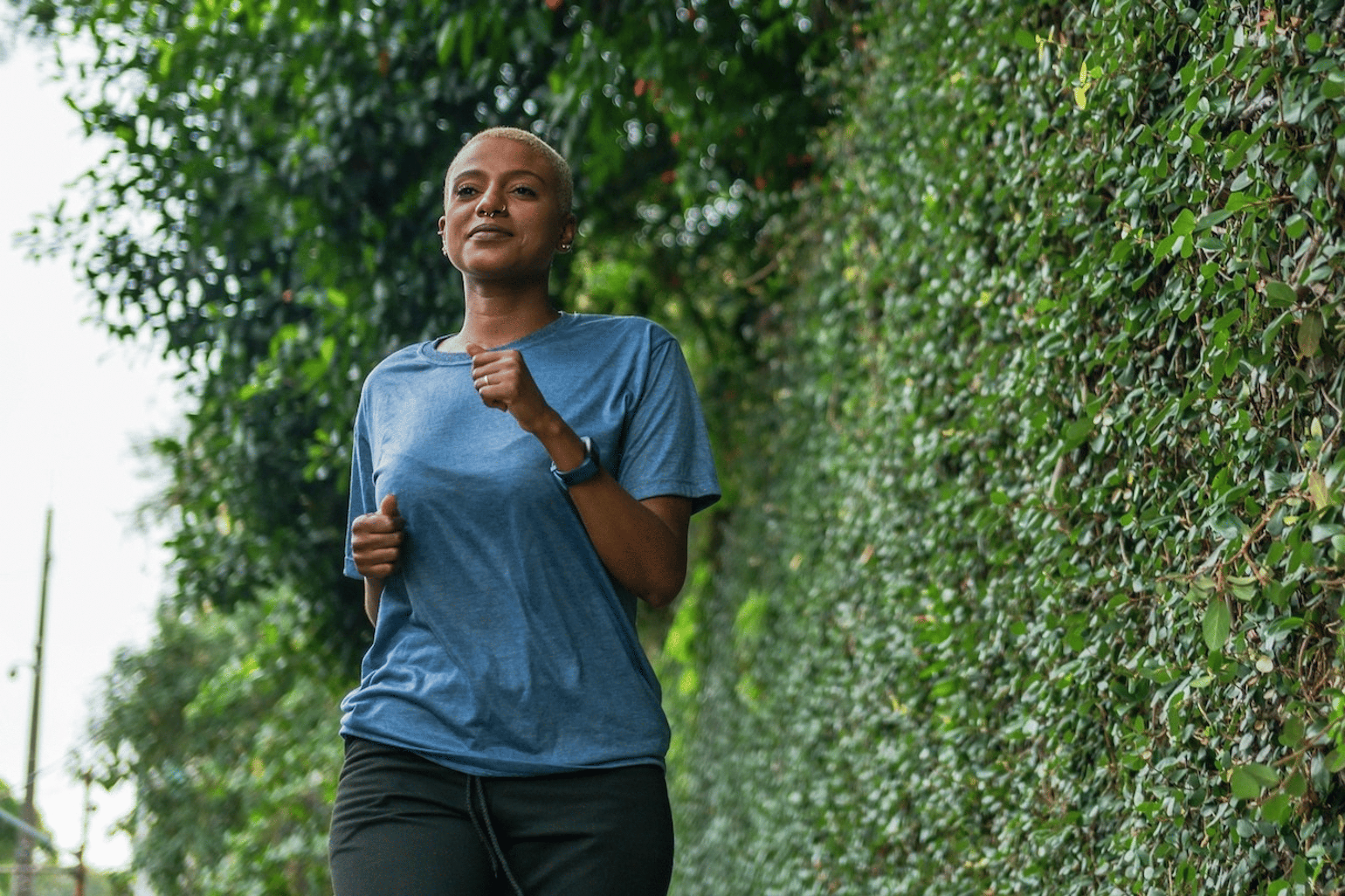 A woman calmly jogging outside near a tall green bush.