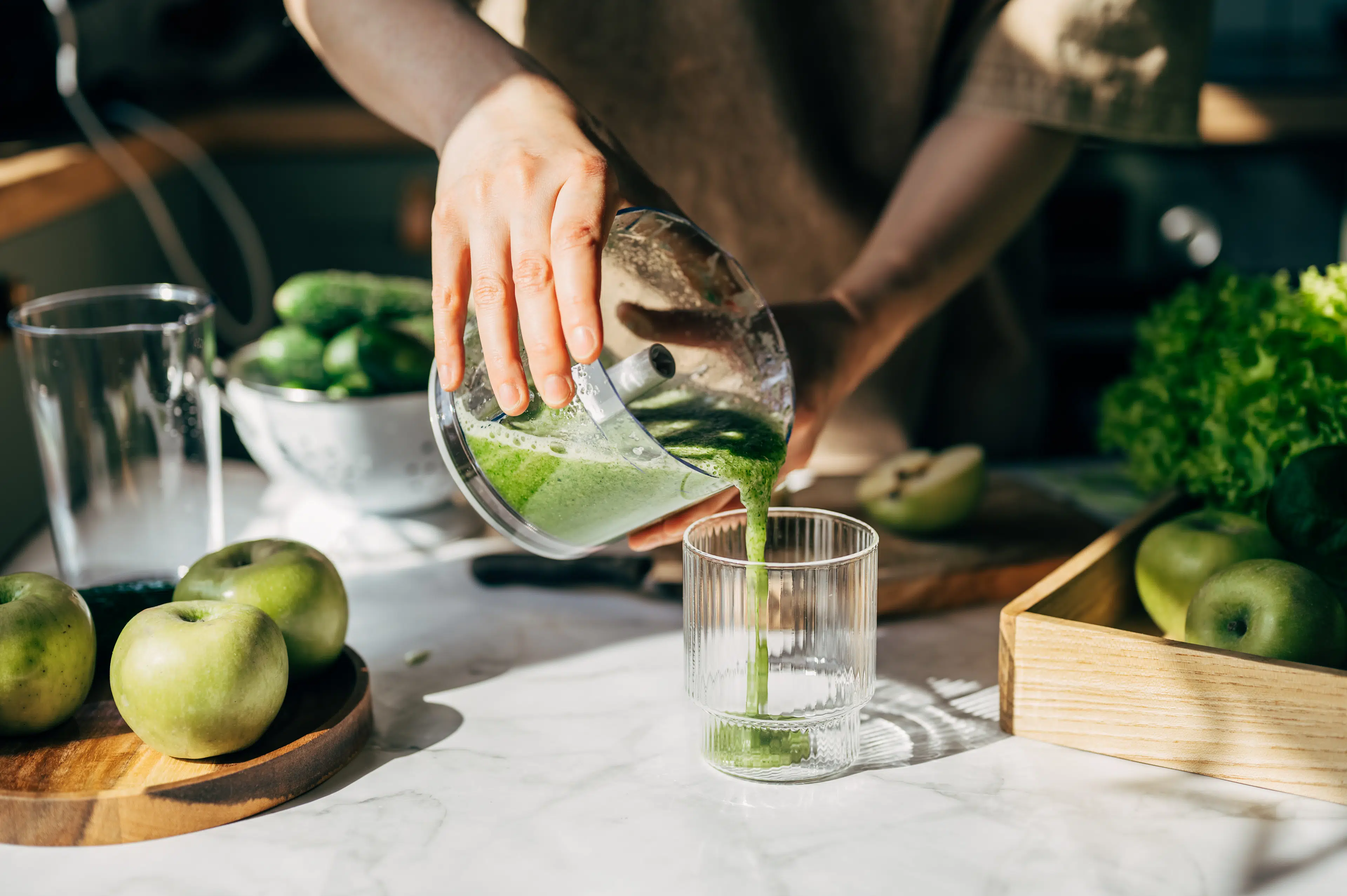 A person pouring a green smoothie from a blender into a glass to help them stay hydrated.