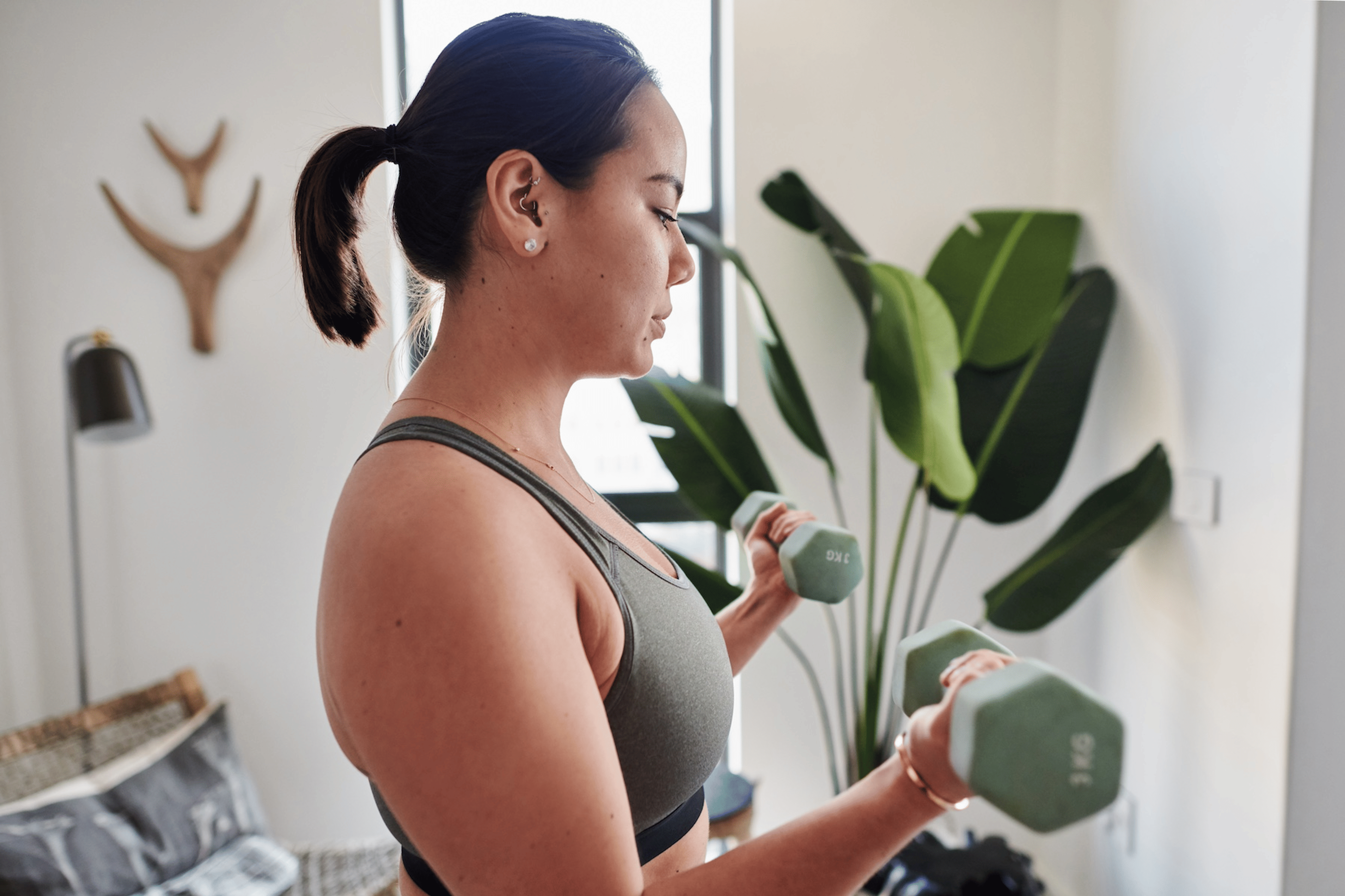 A young woman lifting dumbbells at home.