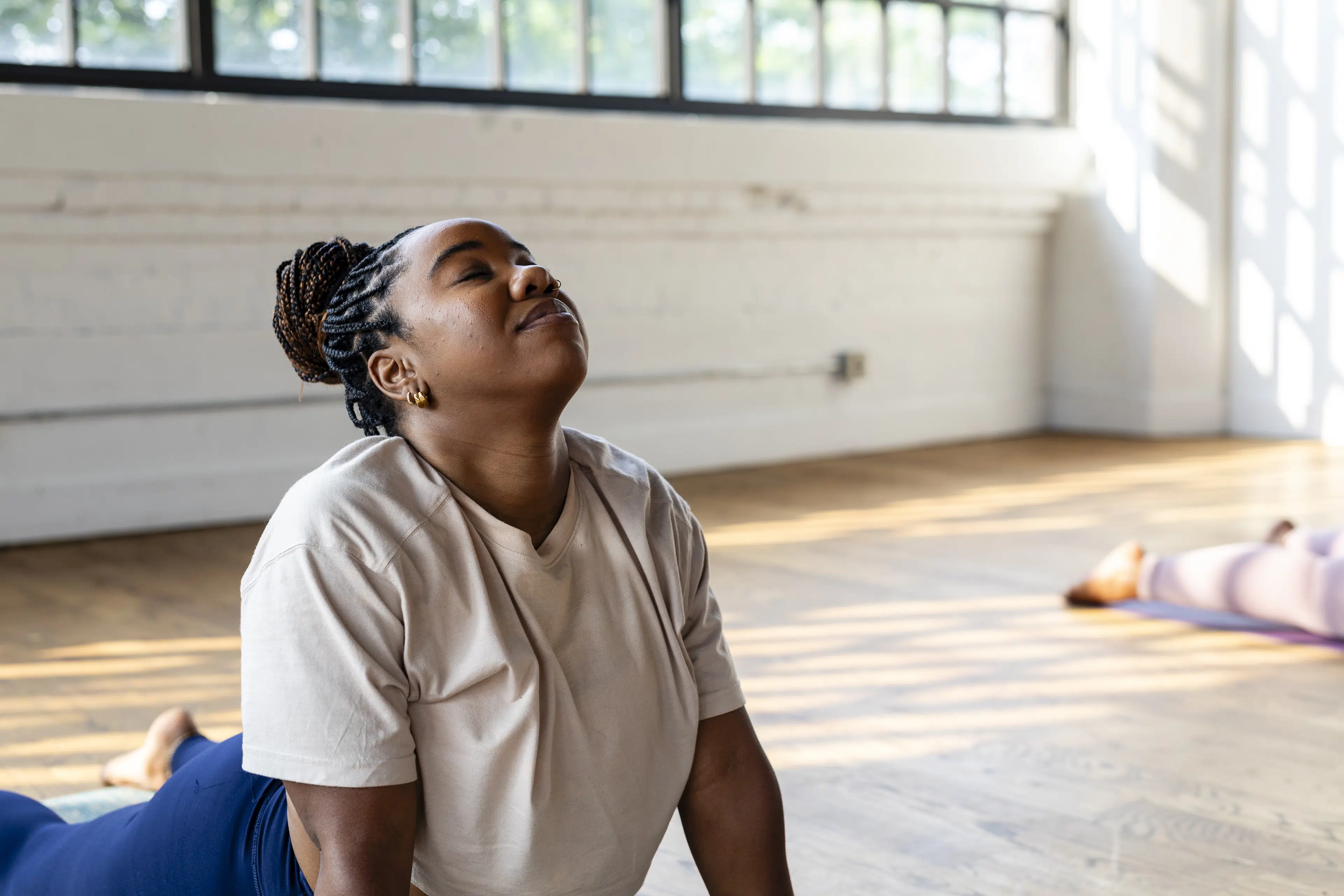 Woman doing easy yoga poses during a yoga class in a bright room on wood floors.