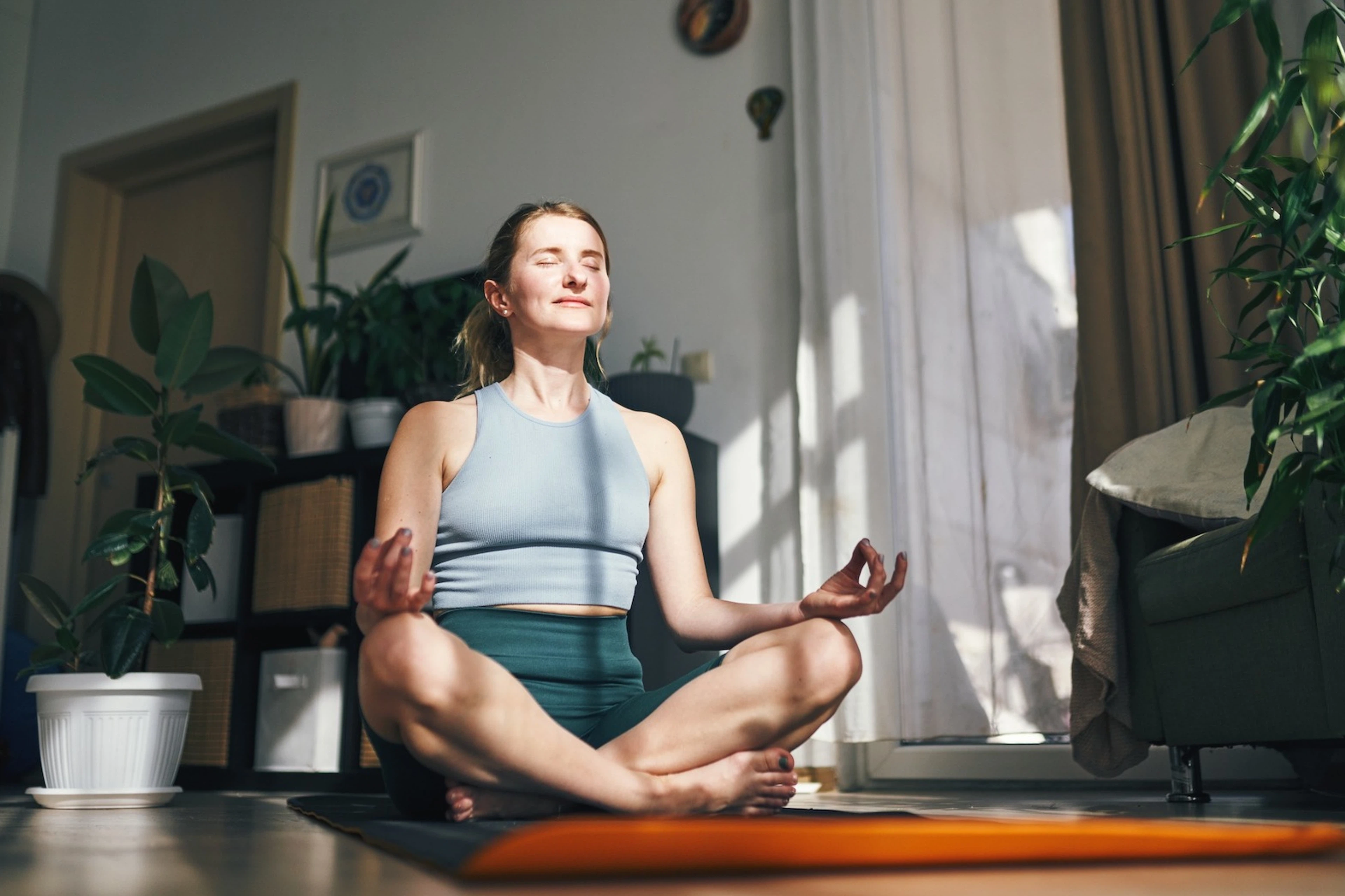 A woman meditating at home in the sunlight as part of her morning routine.
