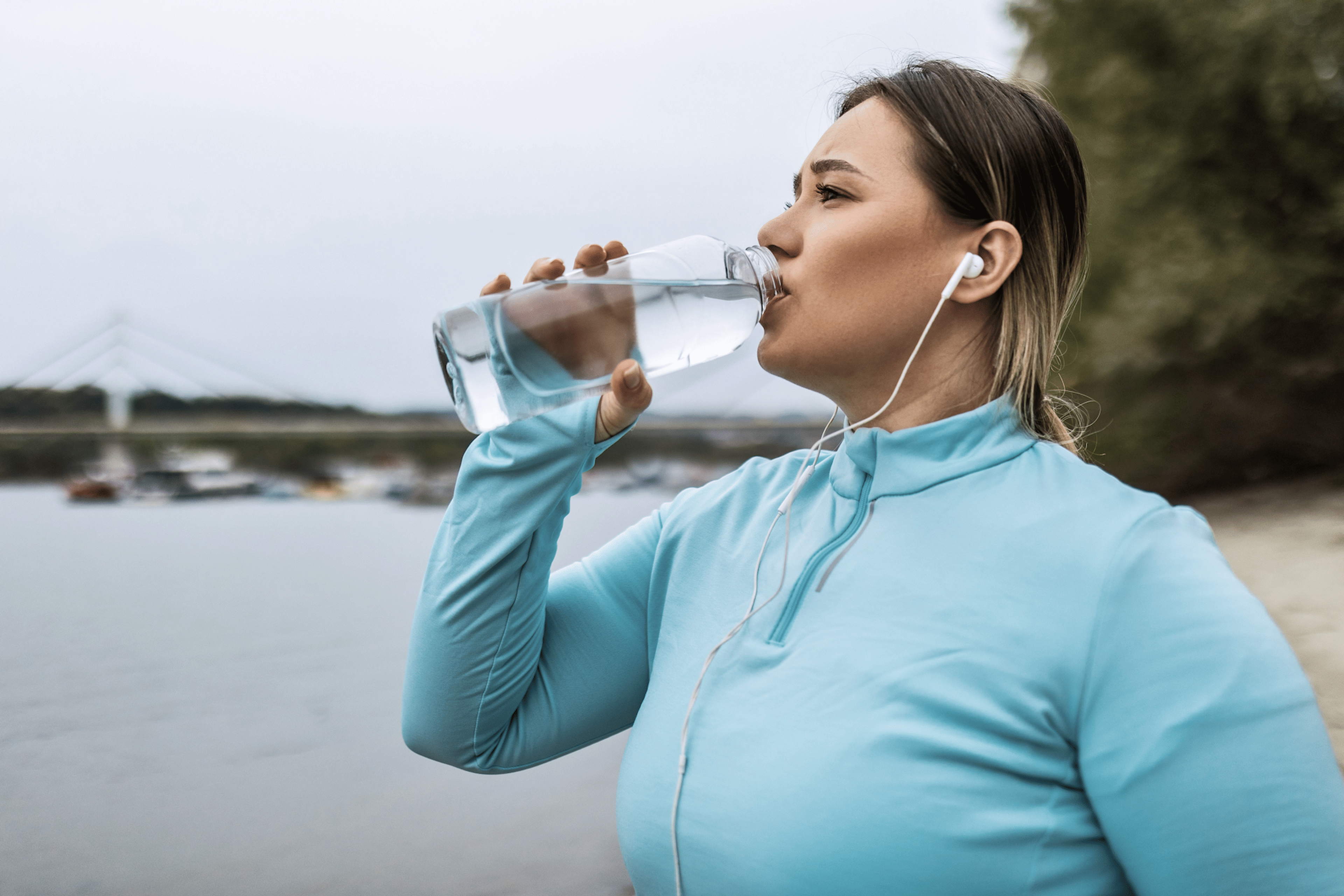 A woman drinking from a clear water bottle during an outdoor workout.