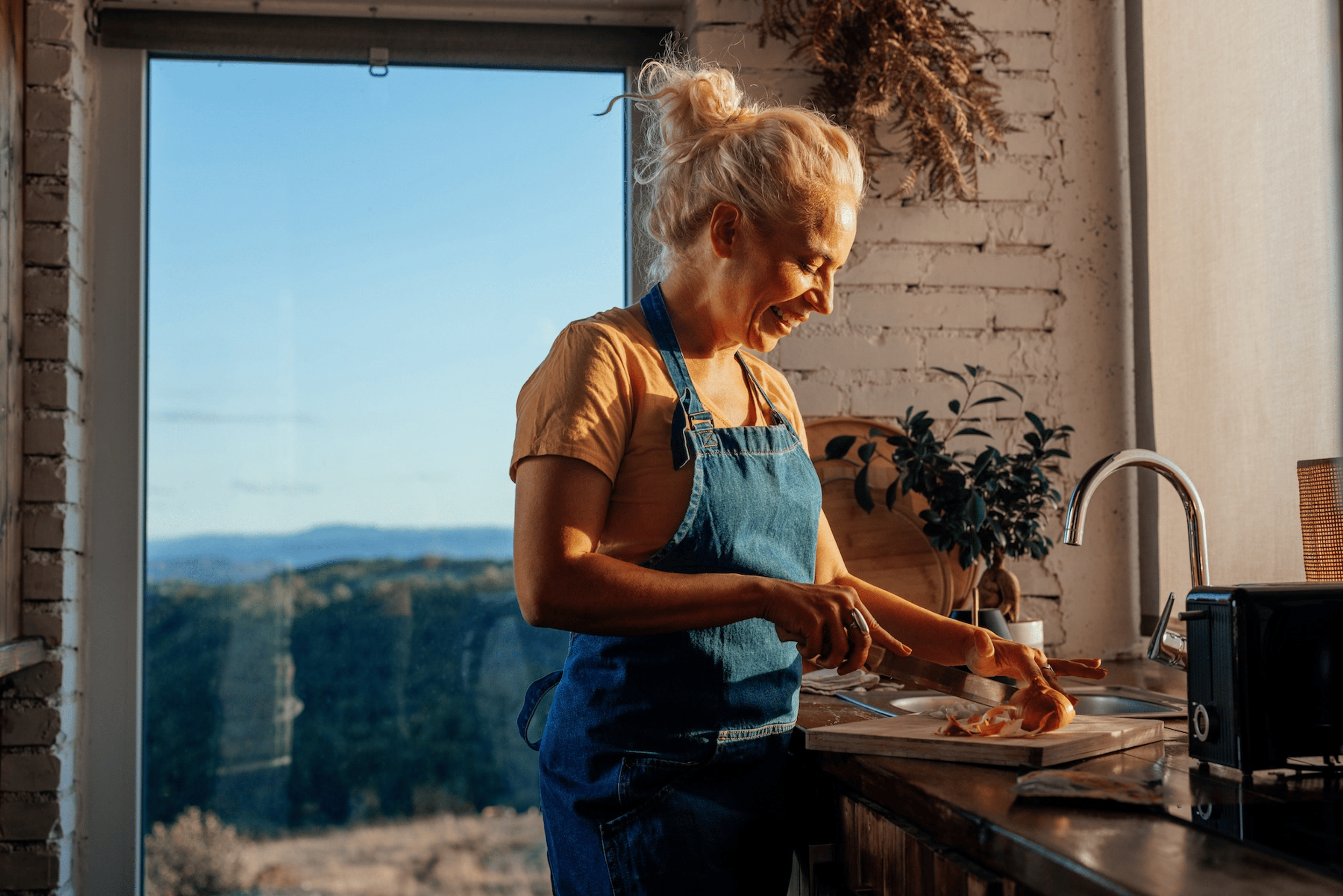 A middle-aged woman making mindful menopause nutrition choices by making a healthy salad. She's standing in her modern kitchen and chopping an onion.