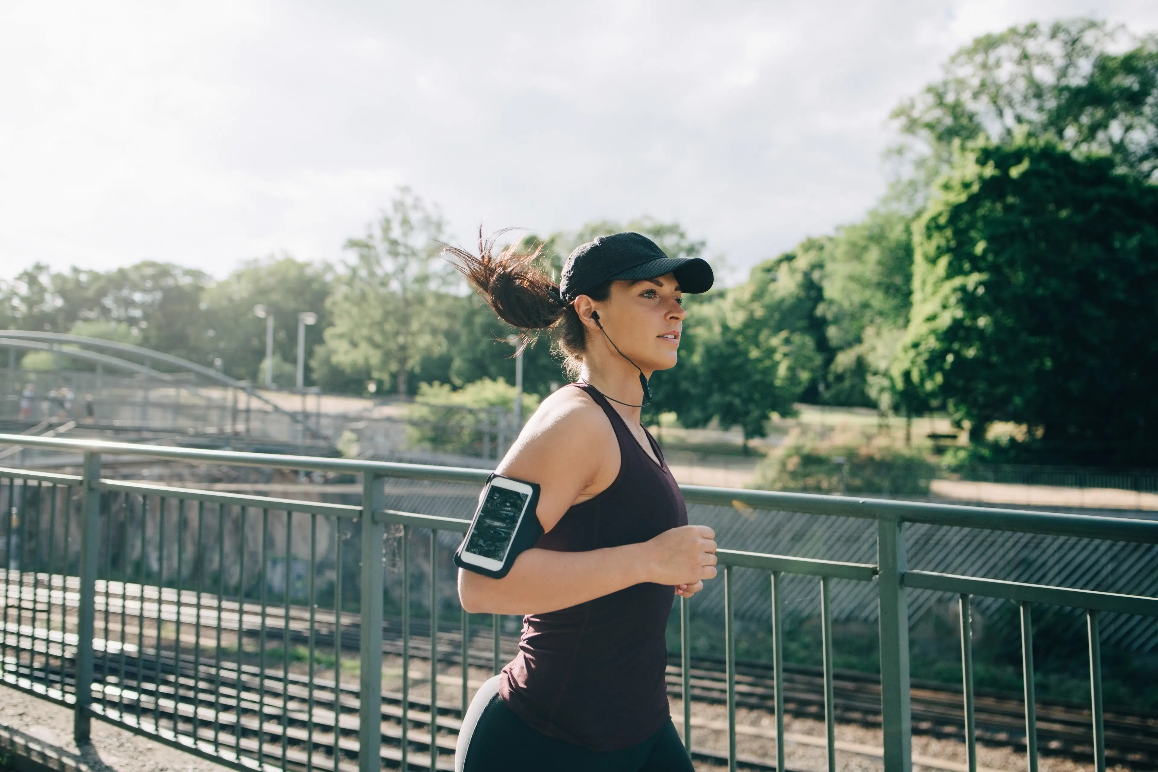 Woman jogging outside with black baseball cap and black tank top