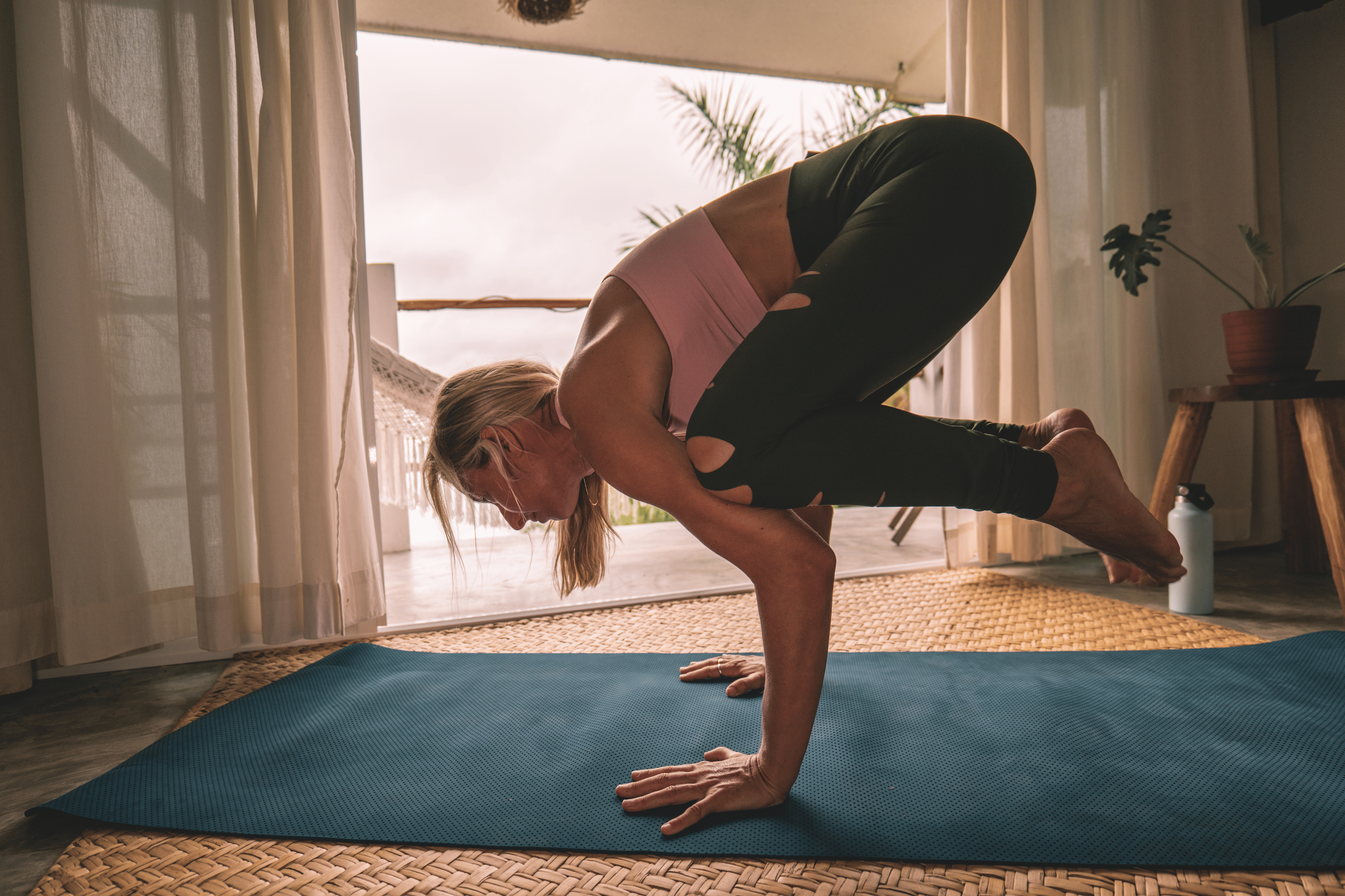 Woman practicing Crow Pose on a mat while doing yoga at home.