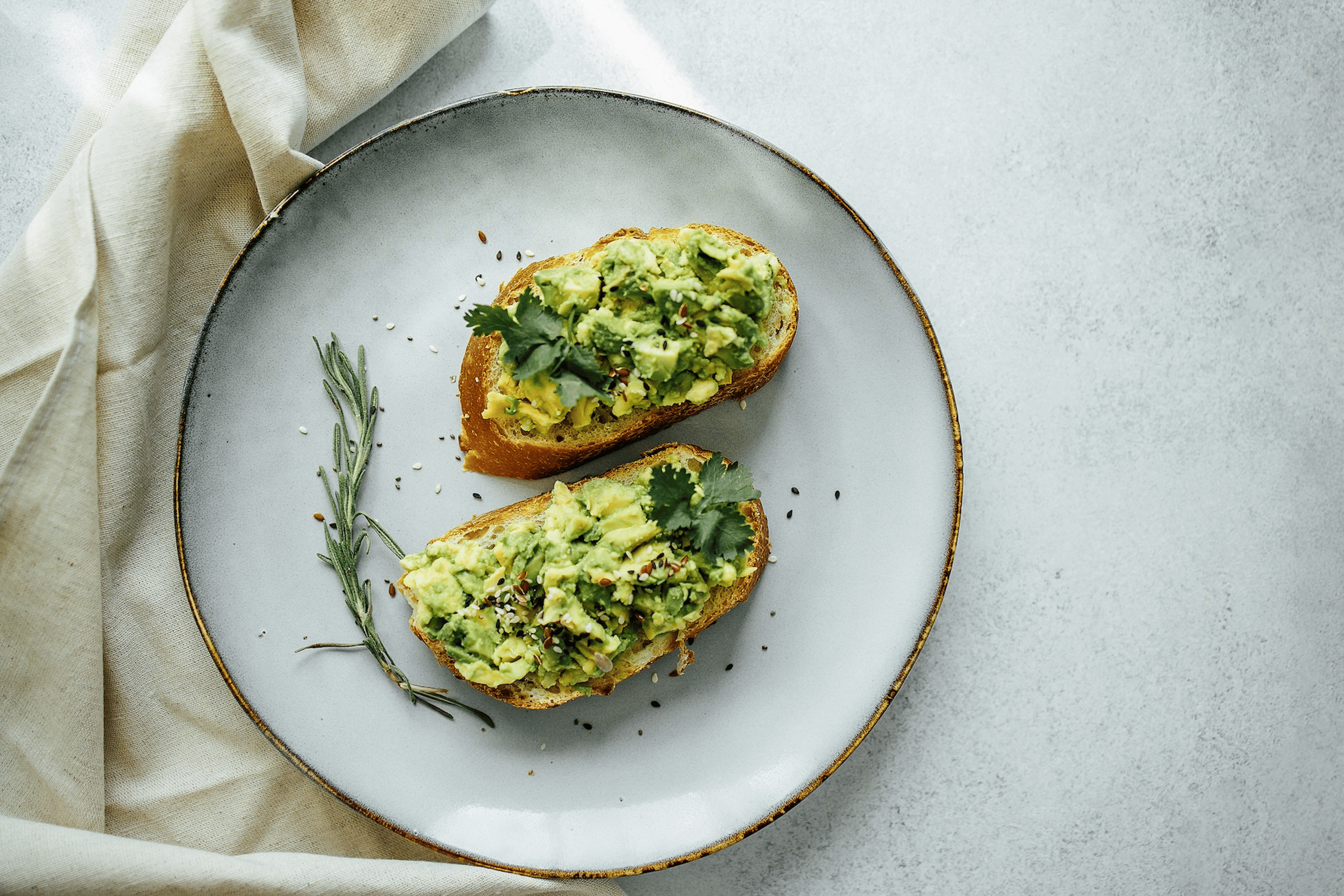 An overhead photo of two pieces of avocado toast garnished with seeds and greens.