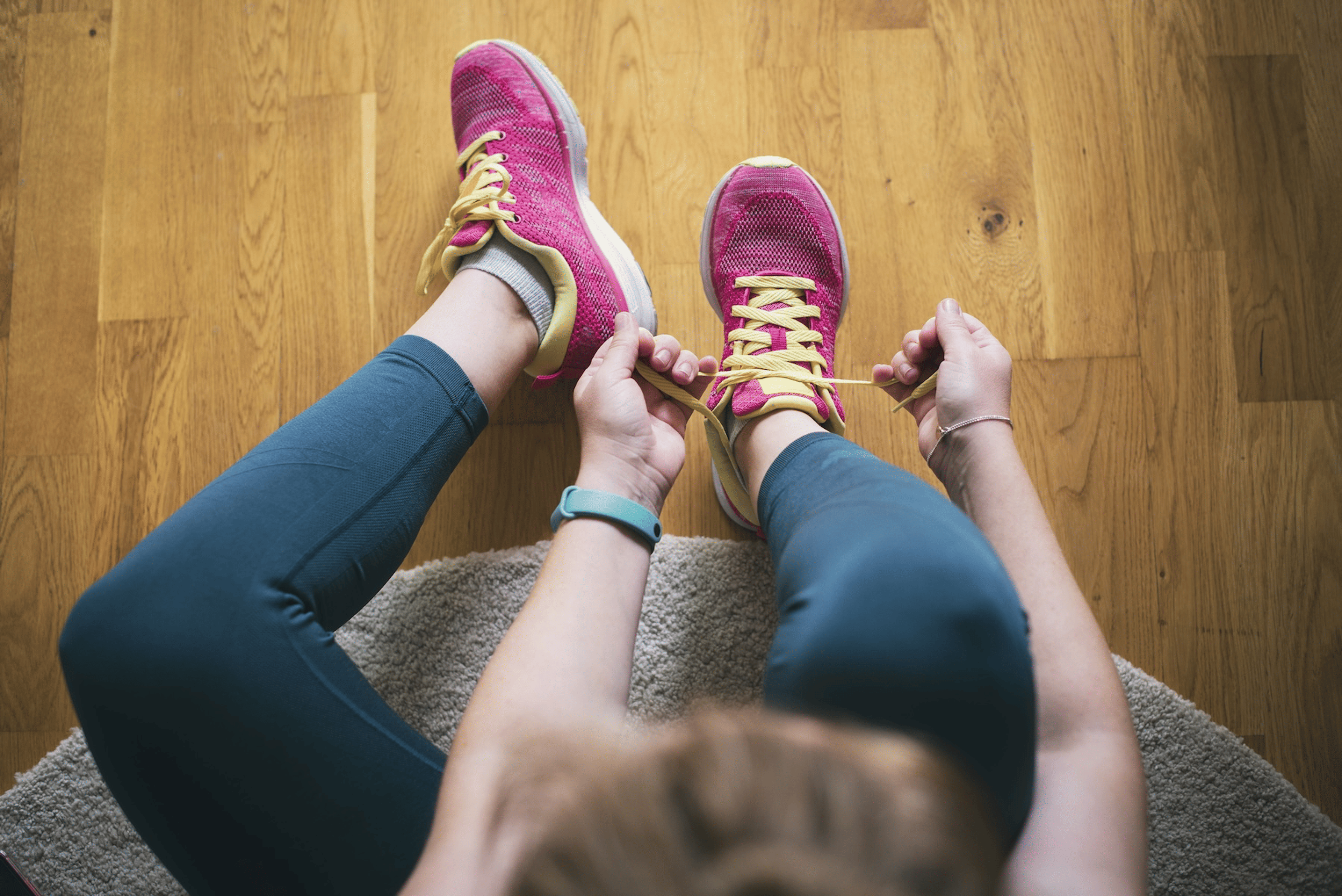 An overhead, close-up view of a woman tying her running shoes. She is practicing self-discipline for exercise by getting ready to work out even if she doesn't want to.