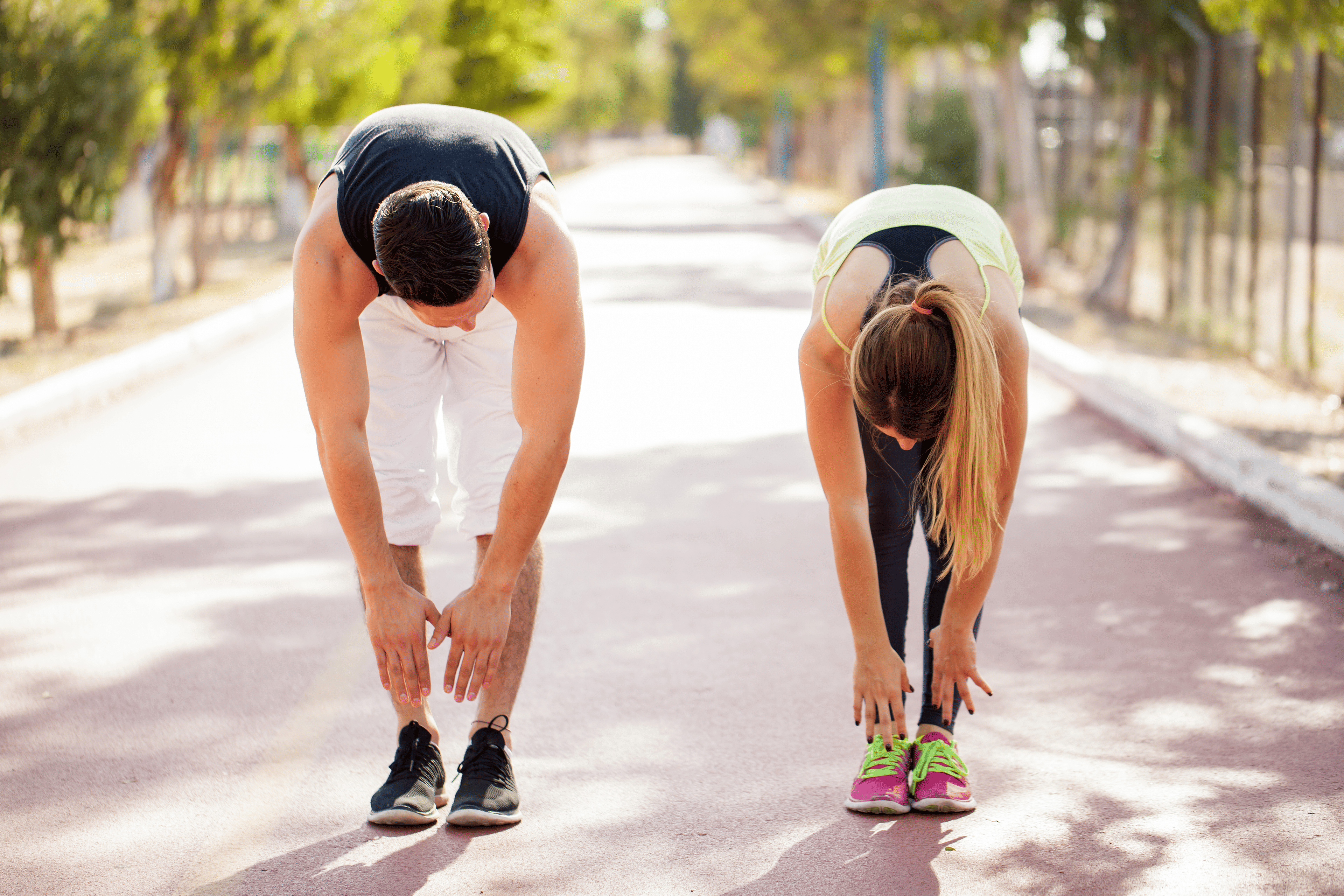 Am man and a woman stretch together outdoors, a toe touch stretch