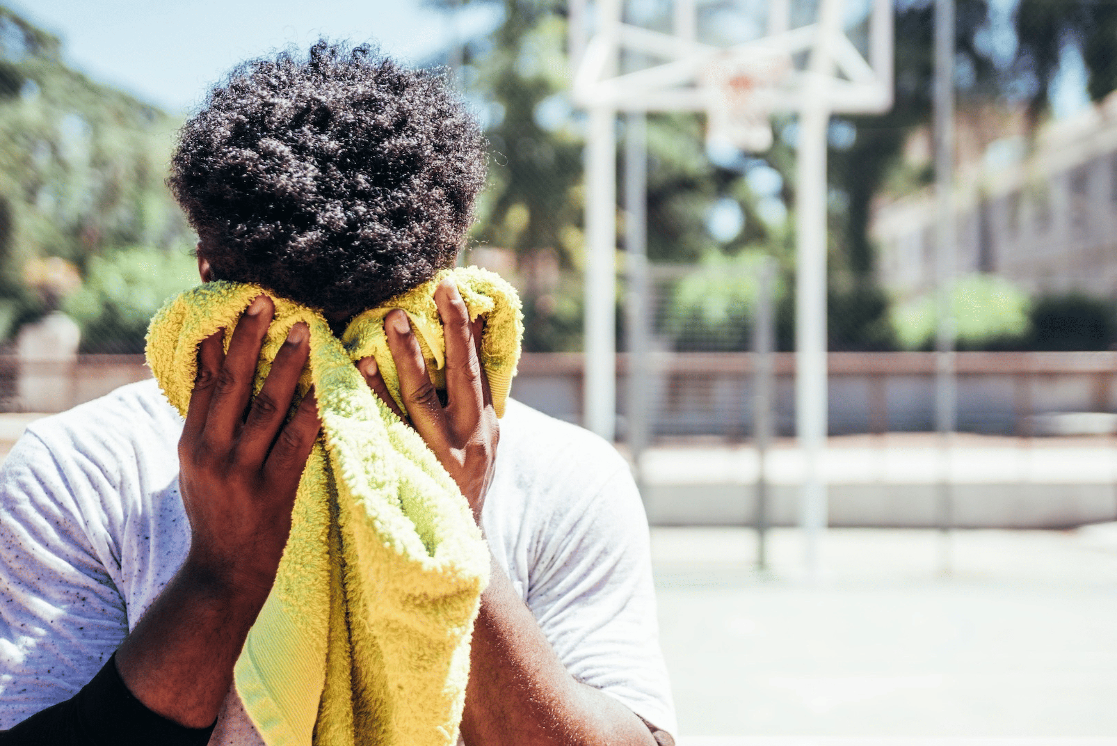 A man wiping away sweat from his face with a clean towel after an outdoor basketball game to prevent sweat pimples.