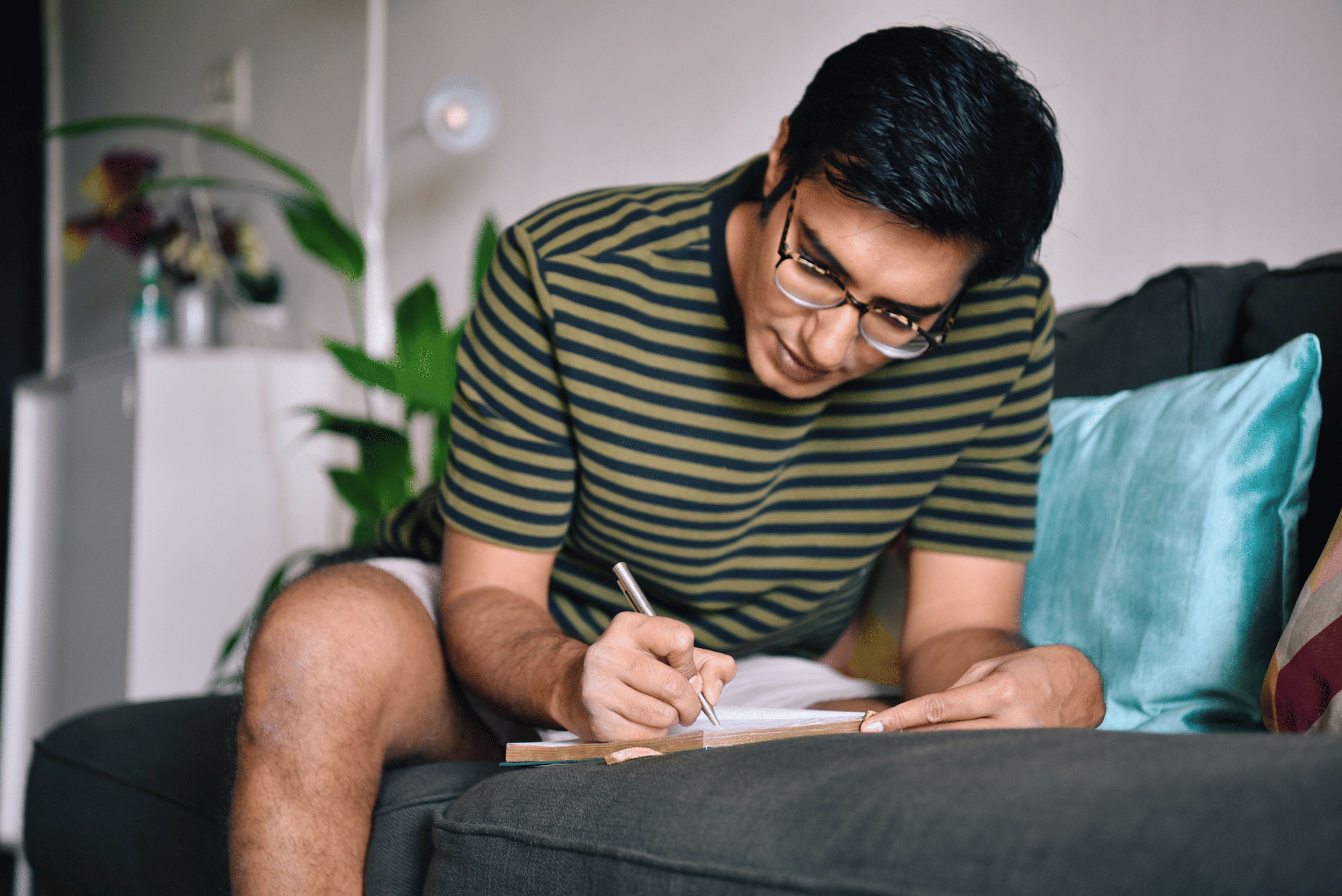 A man sitting on the couch while setting intentions as he writes in his journal.