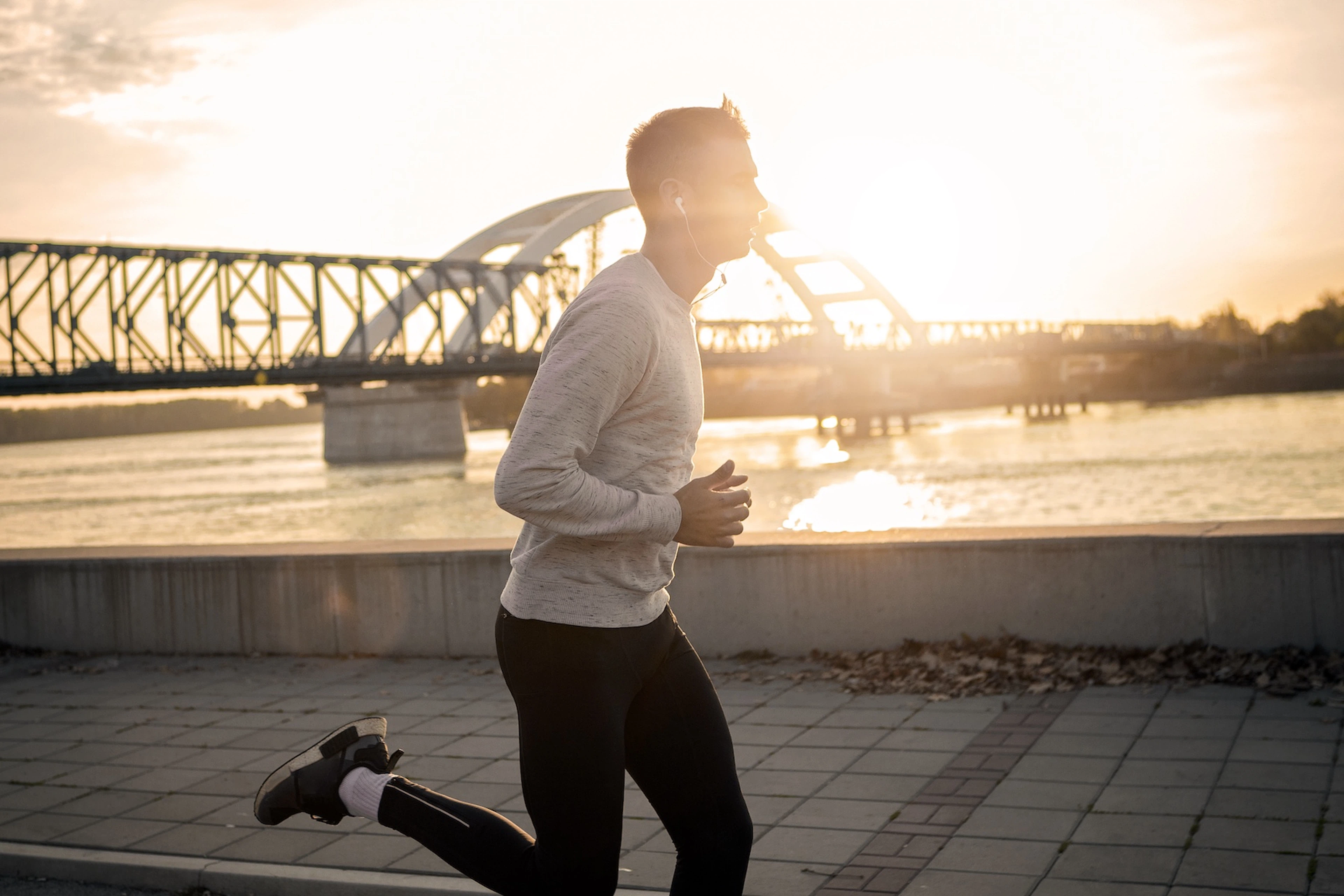 Side view of a man jogging outside near a river in the morning sunlight.