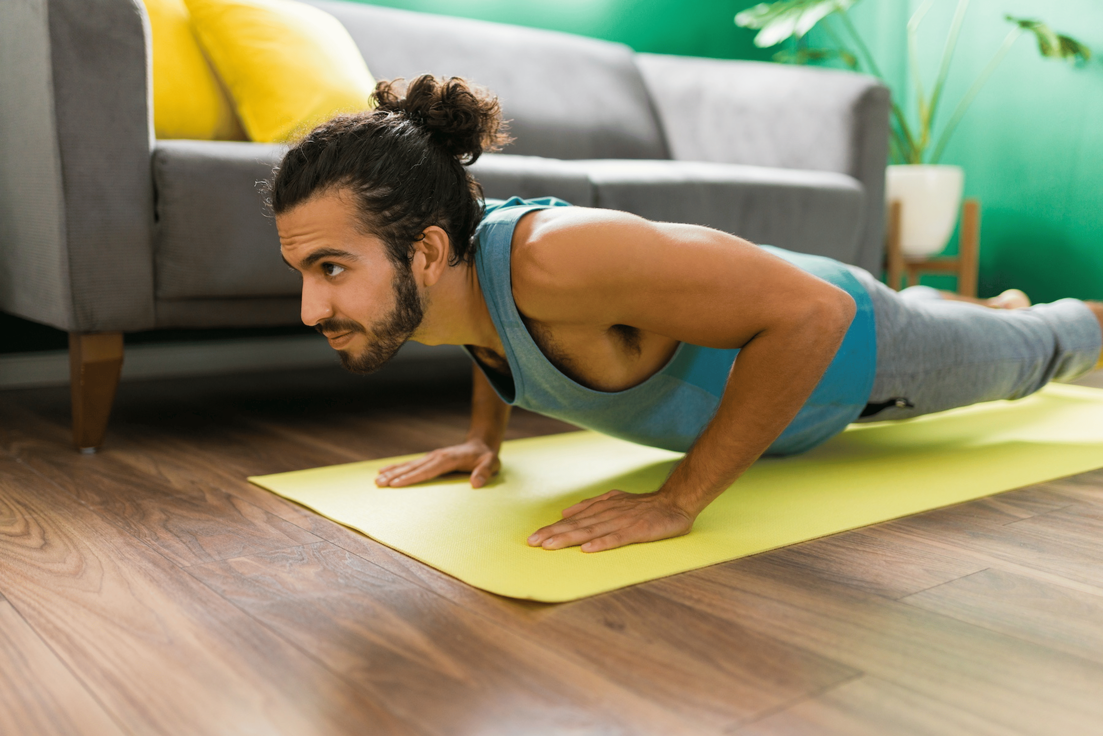 A man in Plank Pose on a yellow yoga mat at home. He is doing yoga to build muscle.