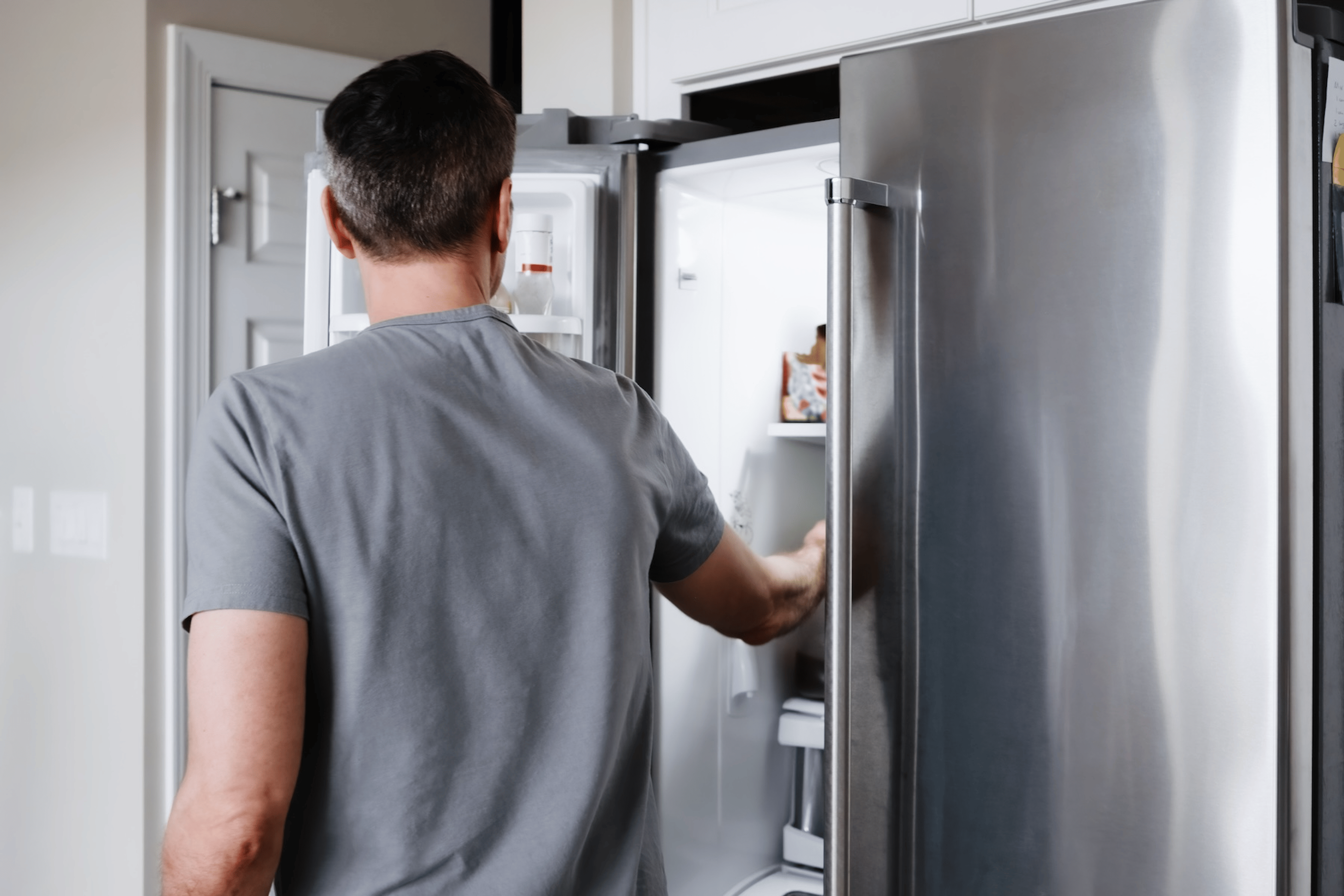 A back view of a man reaching into his fridge for food after a workout.