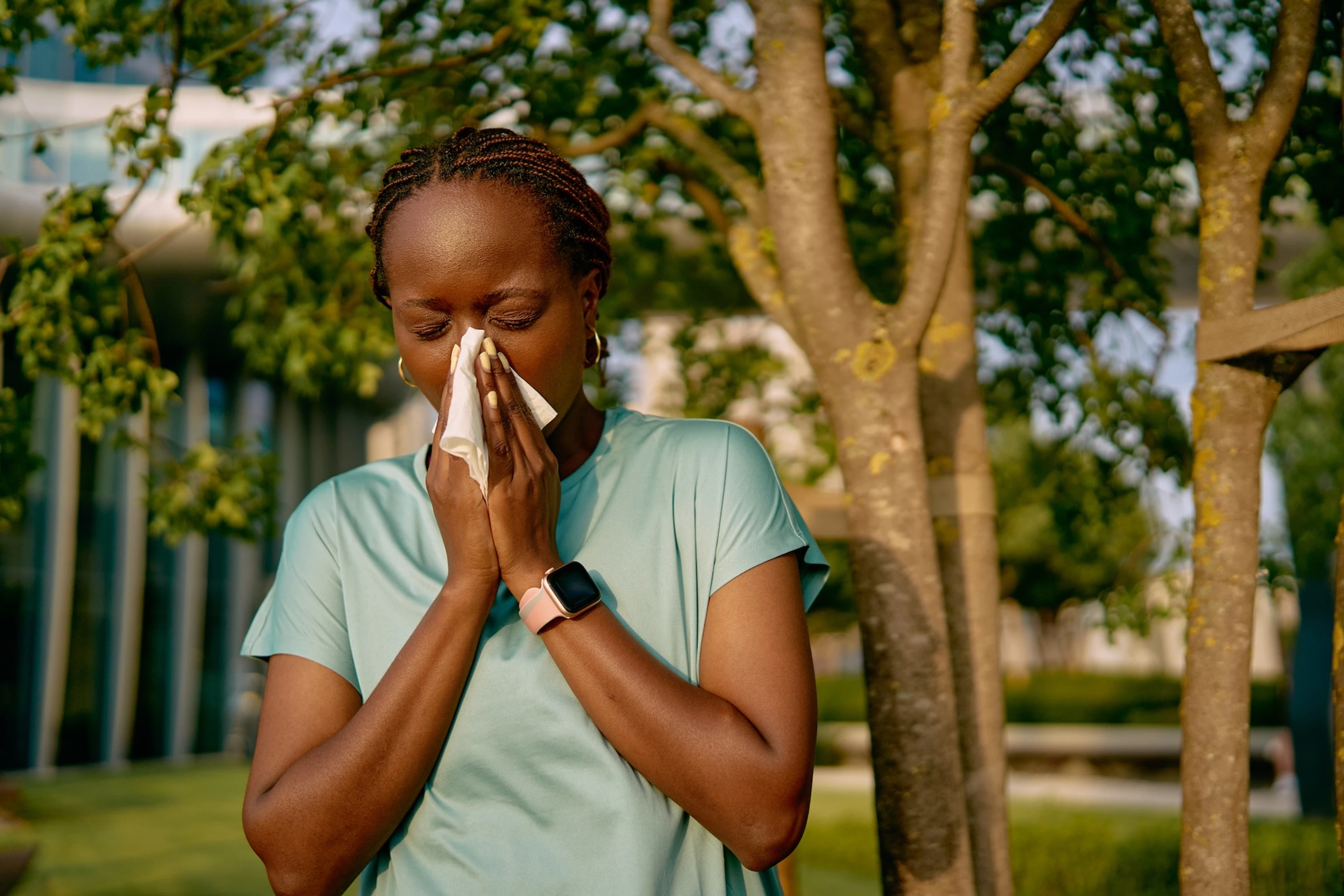A woman blowing her nose into a tissue during an outdoor workout. She's exercising with allergies.