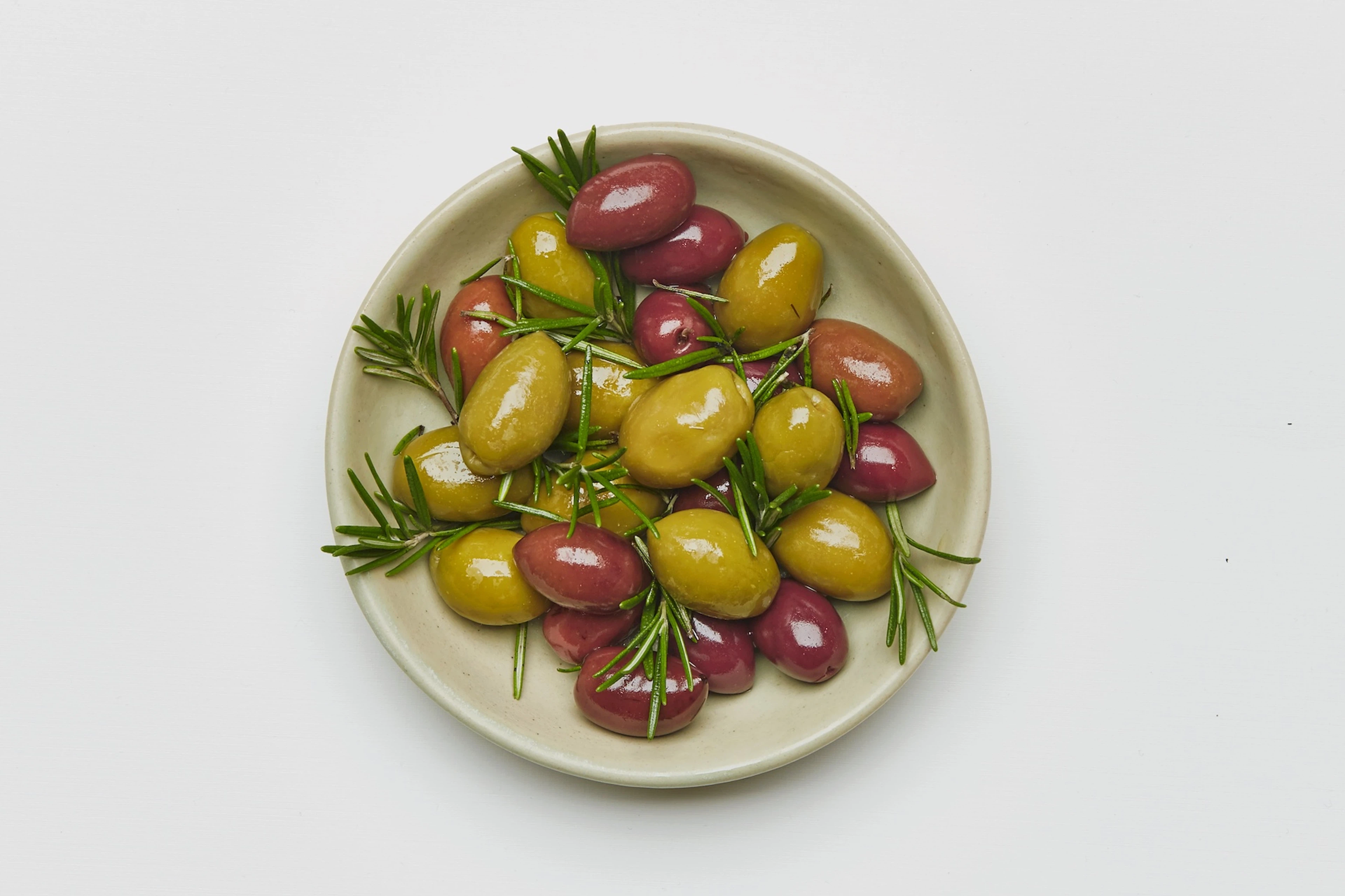 A close-up photo of green and Kalamata olives in a ceramic bowl, garnished with sprigs of rosemary.