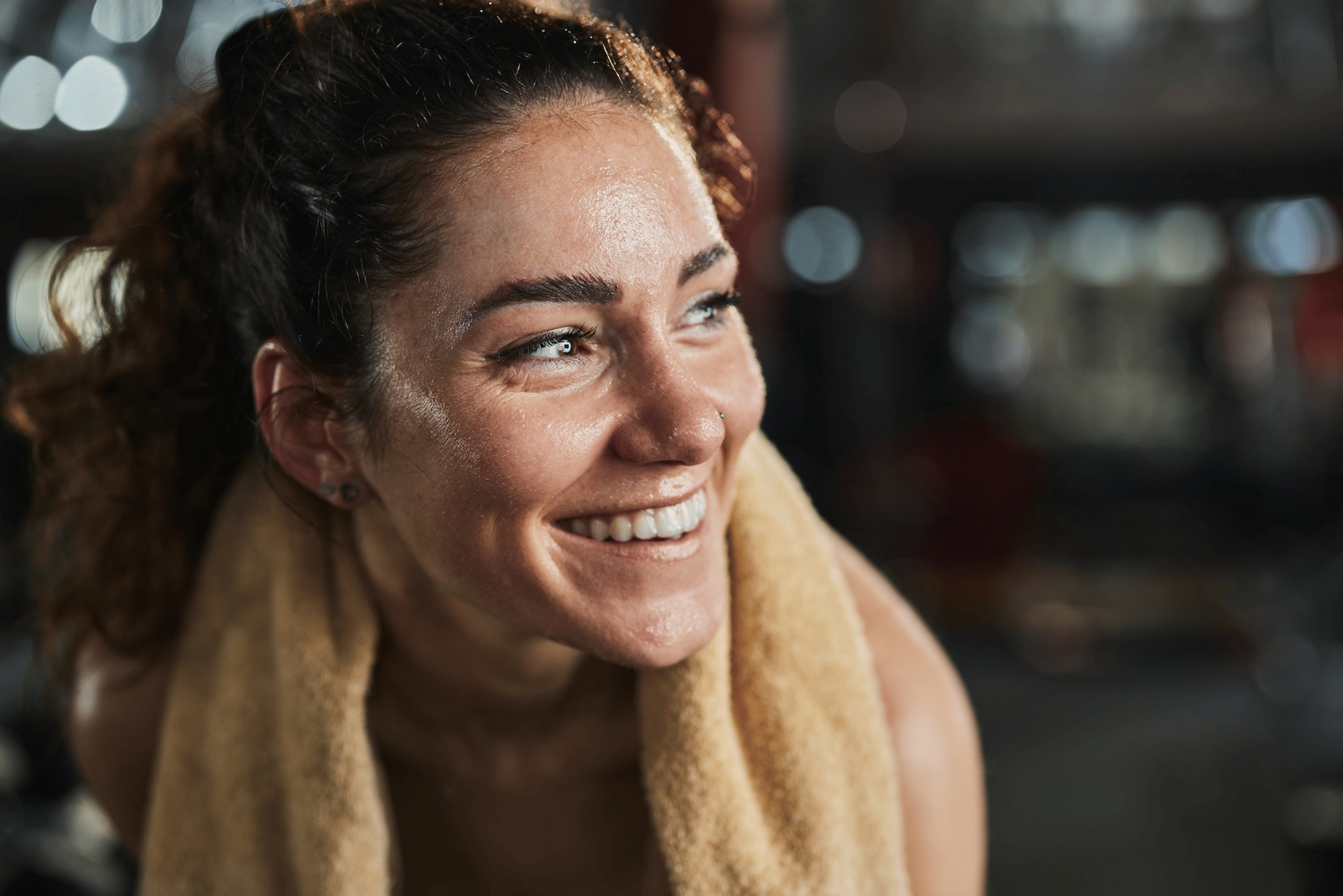 A happy, sweaty athlete smiling and looking to the side. There's a towel around her neck.