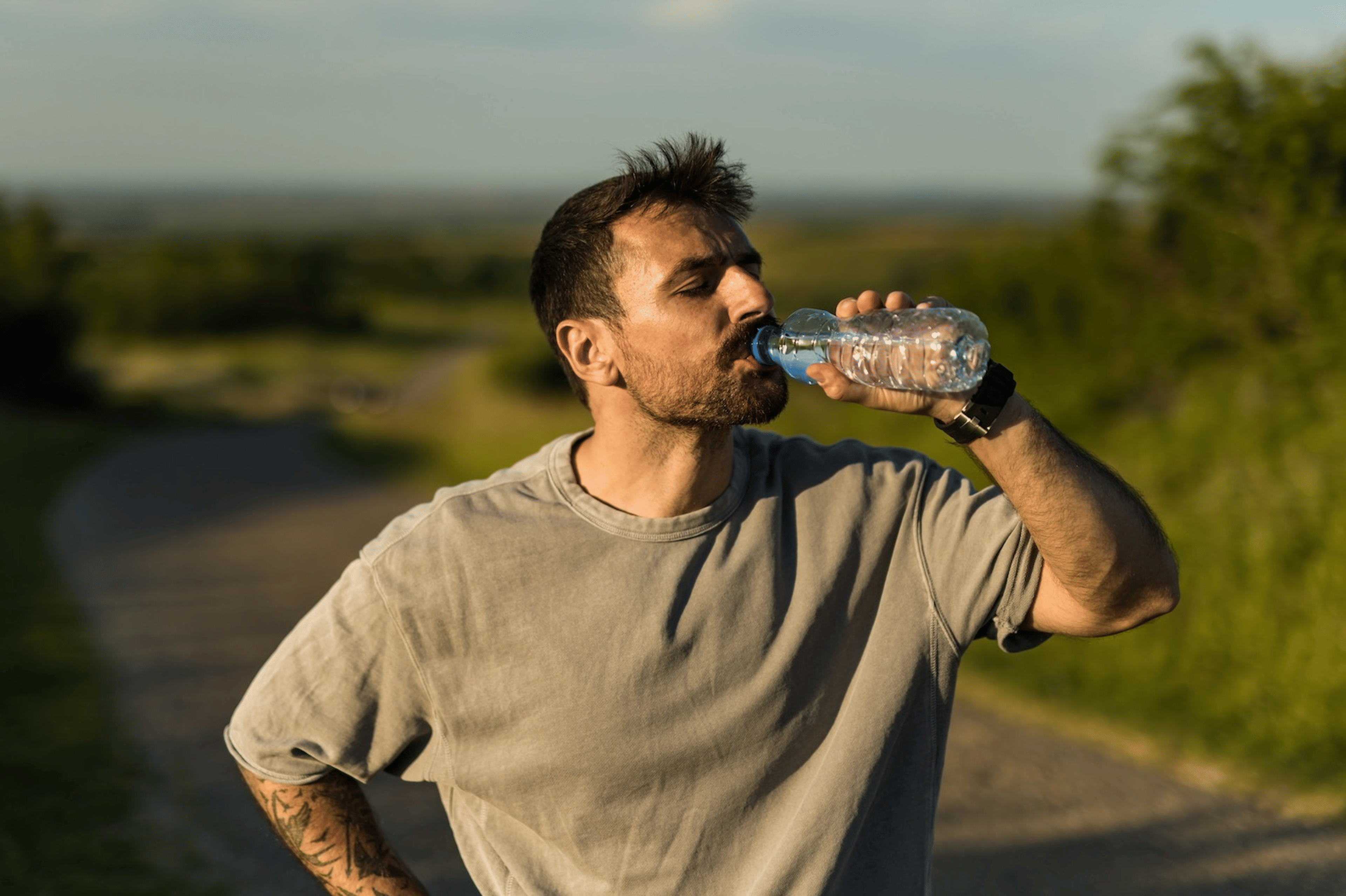 A man drinking water during a workout. He's outside on a sunny day.
