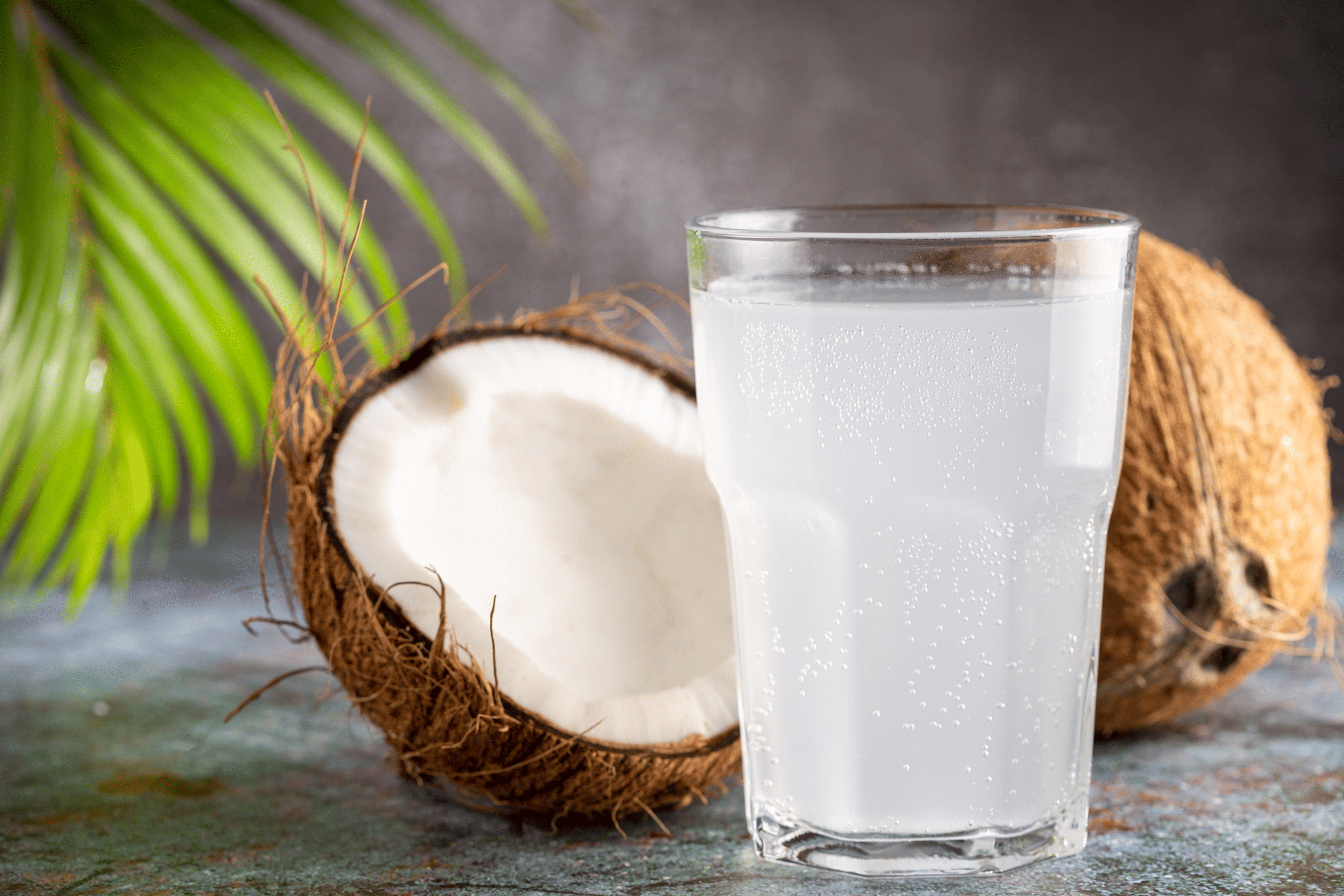 A clear glass of coconut water sitting in front of coconuts. There are many health benefits of coconut water.