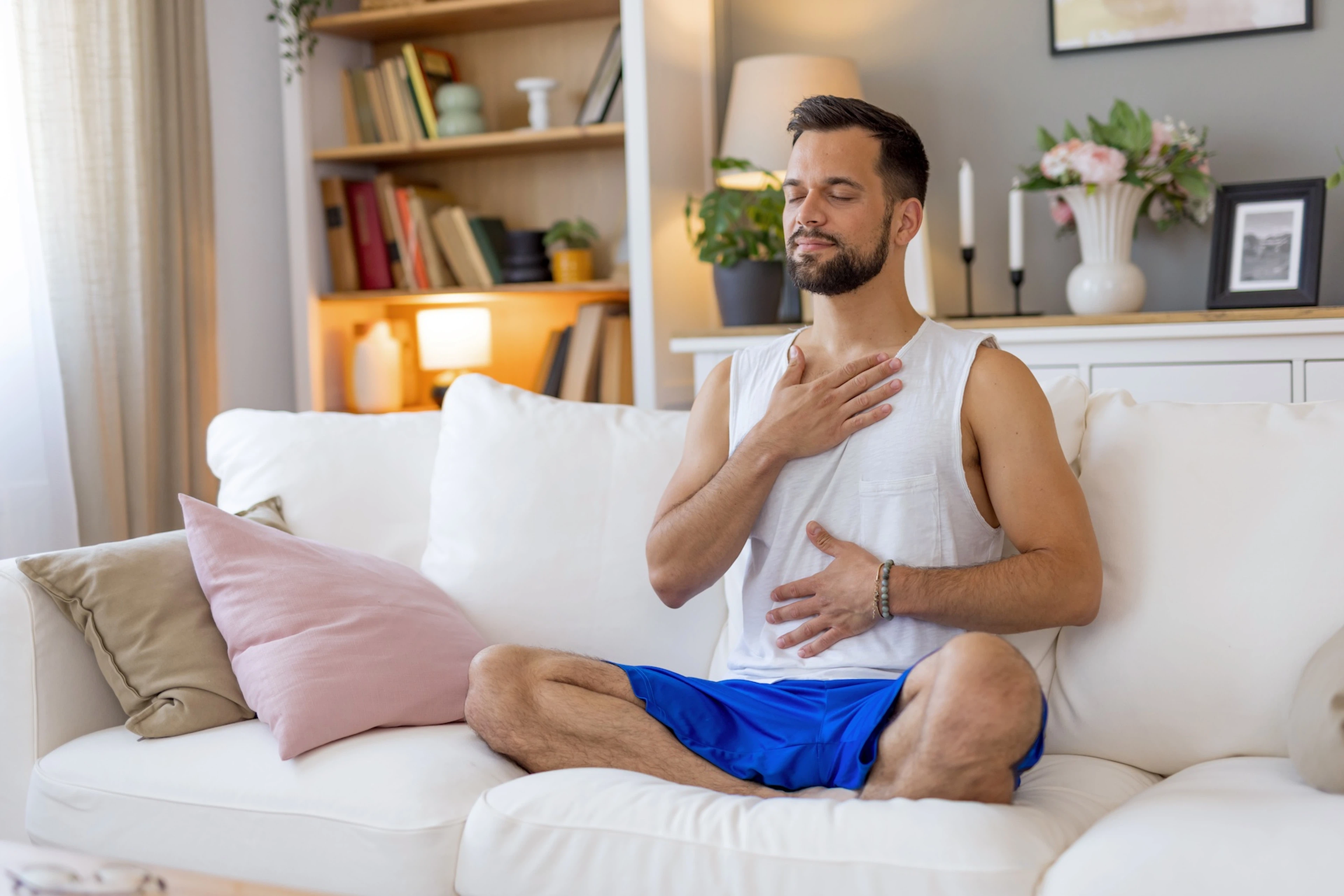 A man practicing gratitude meditation at home on his couch with his hands on his chest and belly.