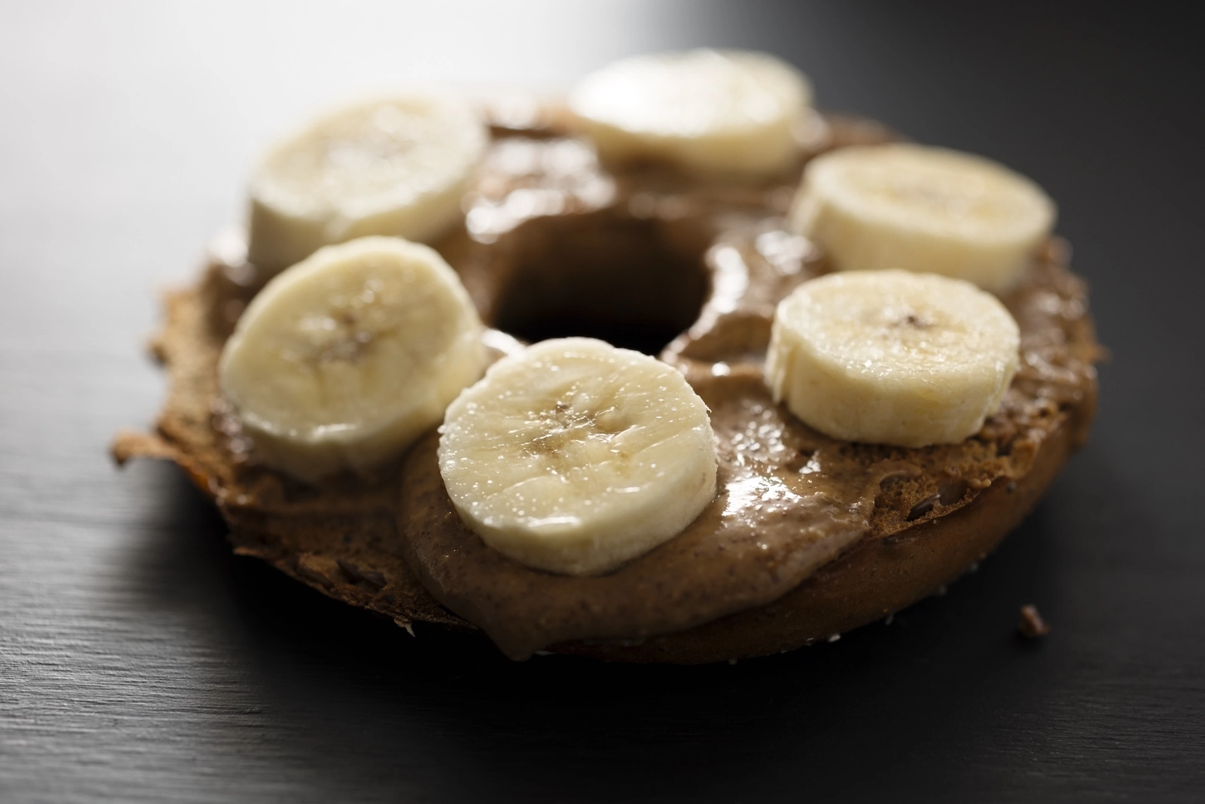 A close-up photo of a bagel with peanut butter and banana slices, an excellent breakfast before a marathon.