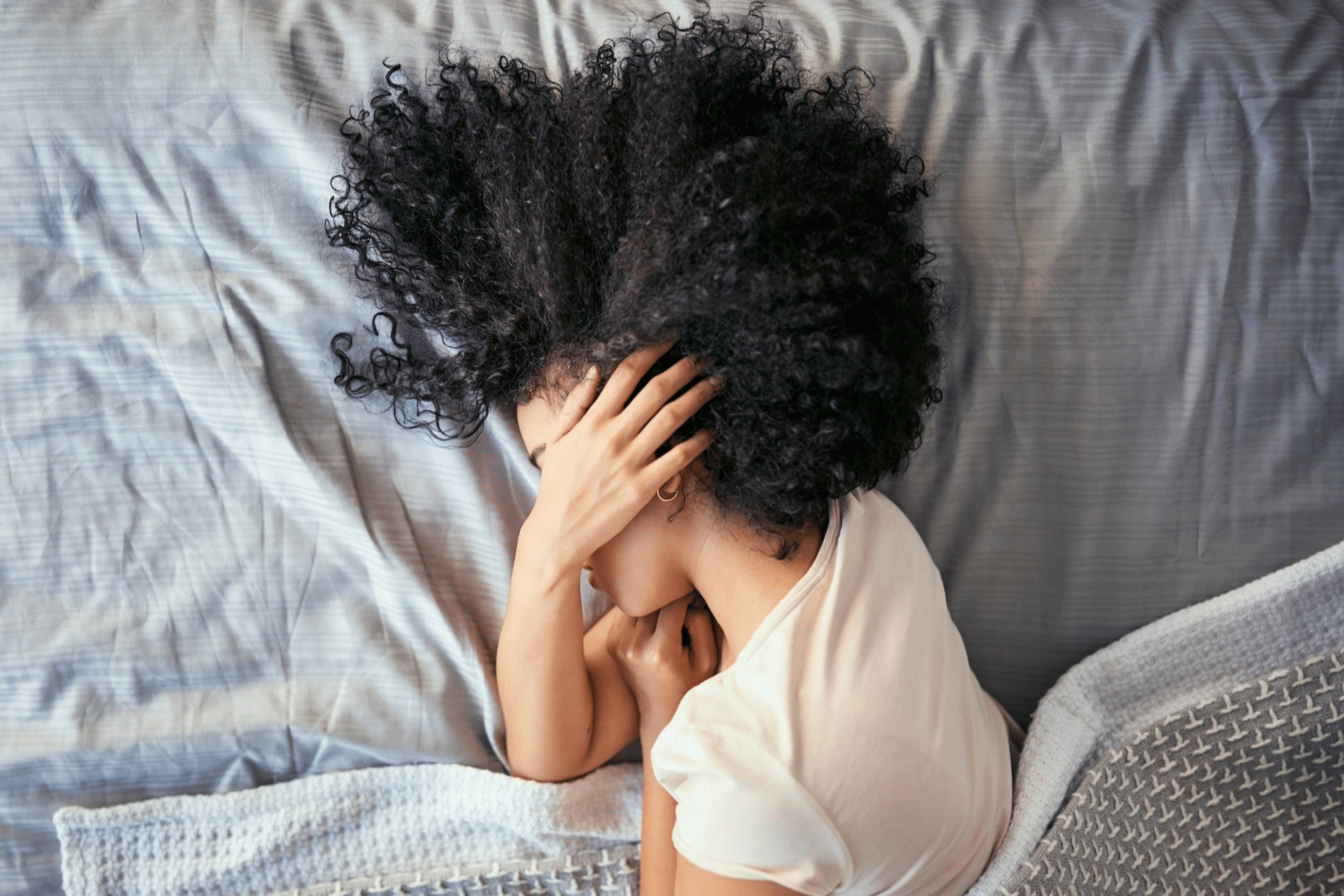 A woman lying in bed on her side as she has morning anxiety. Her hand is covering her face.
