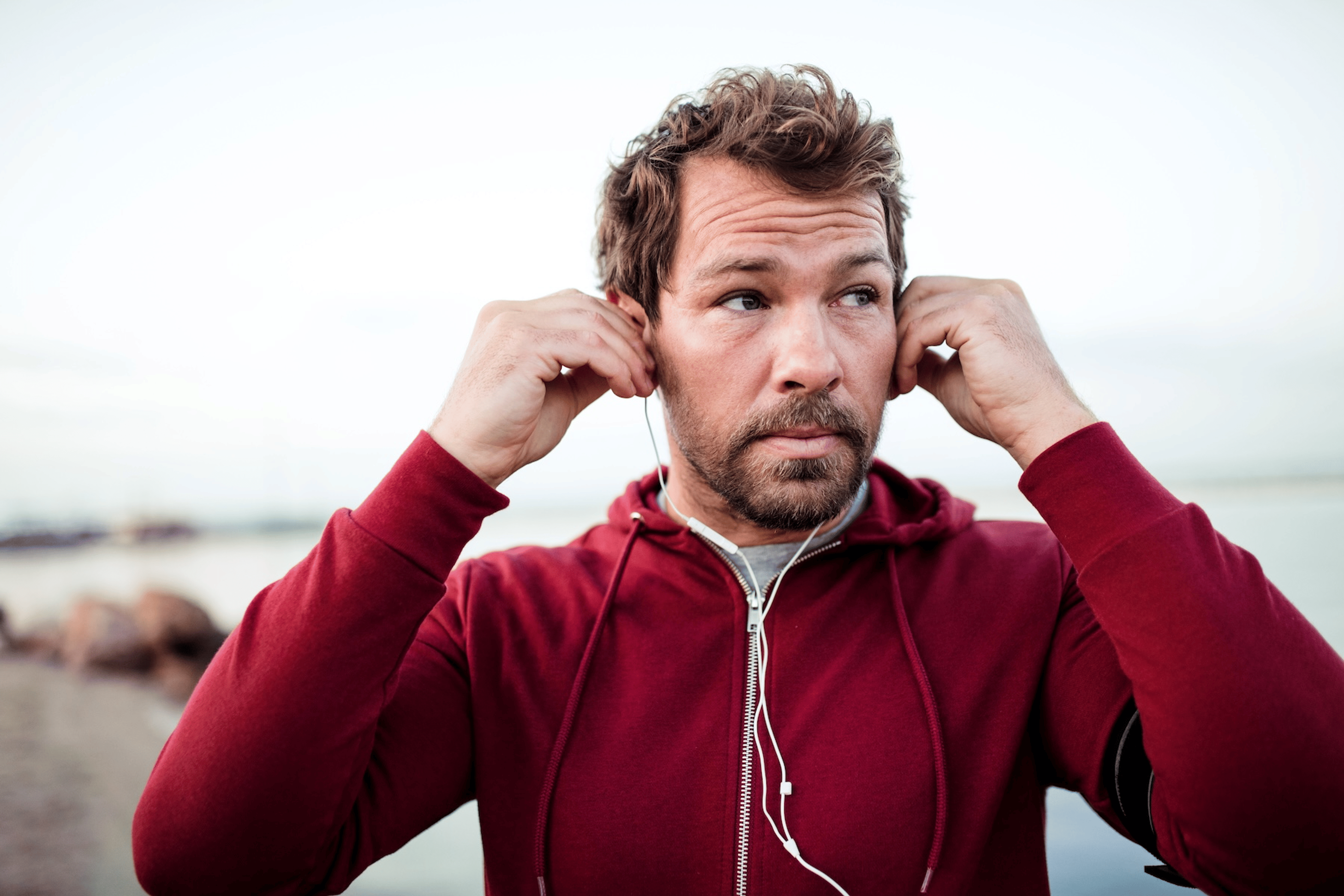 A man holding his ears and adjusting his headphones as he pauses his outdoor run. His ears are hurting while running.