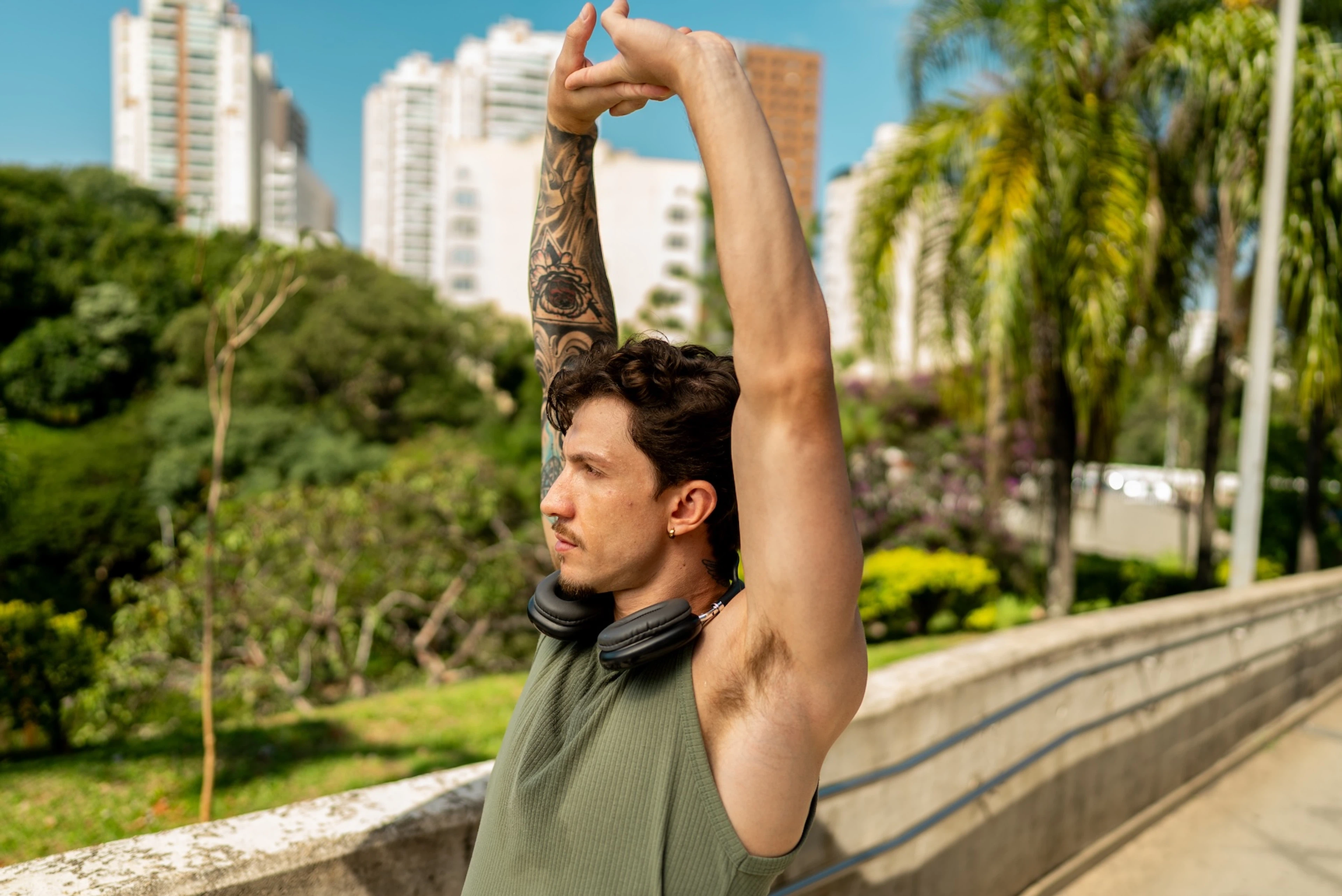 A man working out outside on a sunny day, stretching his arms up overhead.