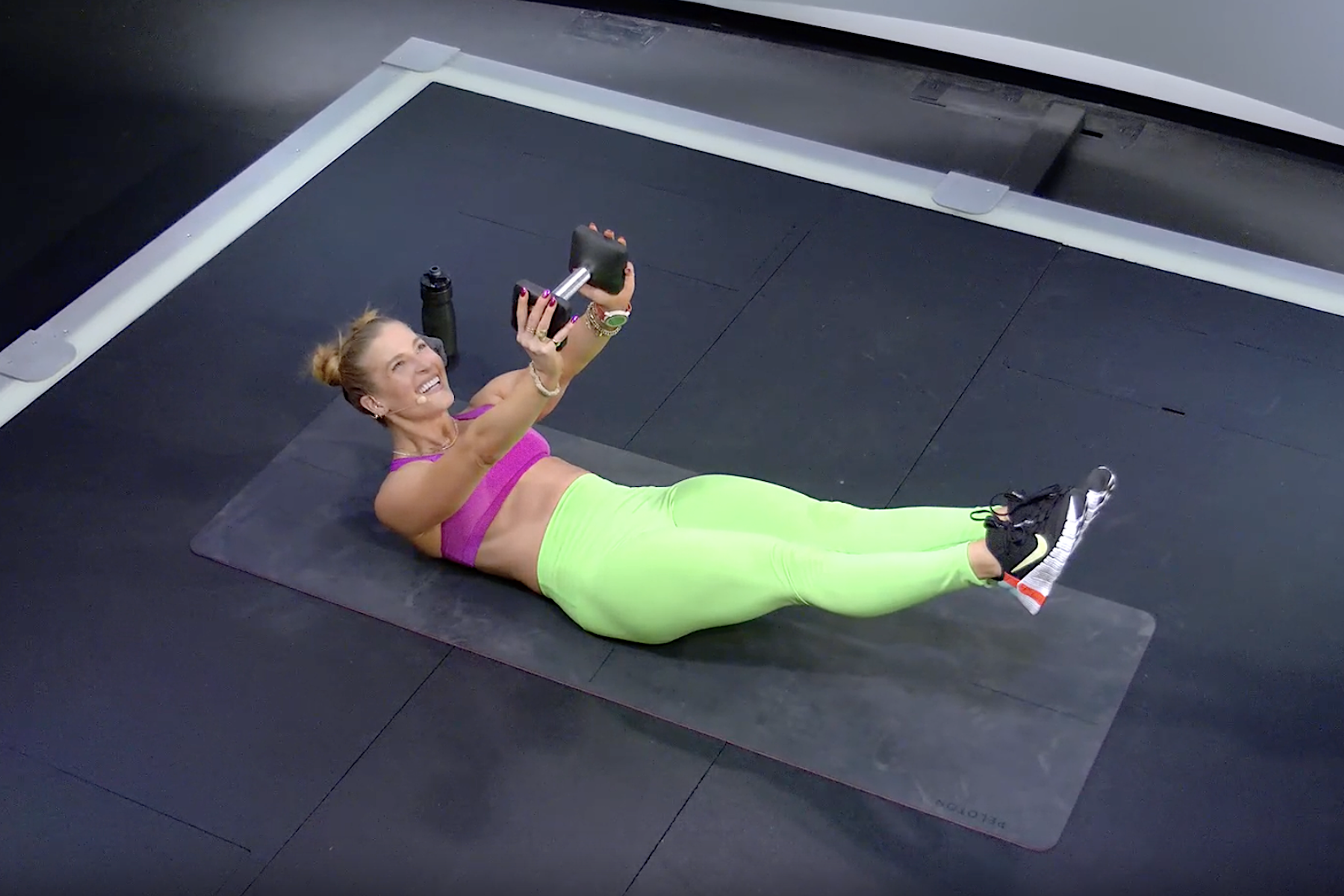 Rebecca Kennedy doing a hollow body hold while holding a dumbbell 
