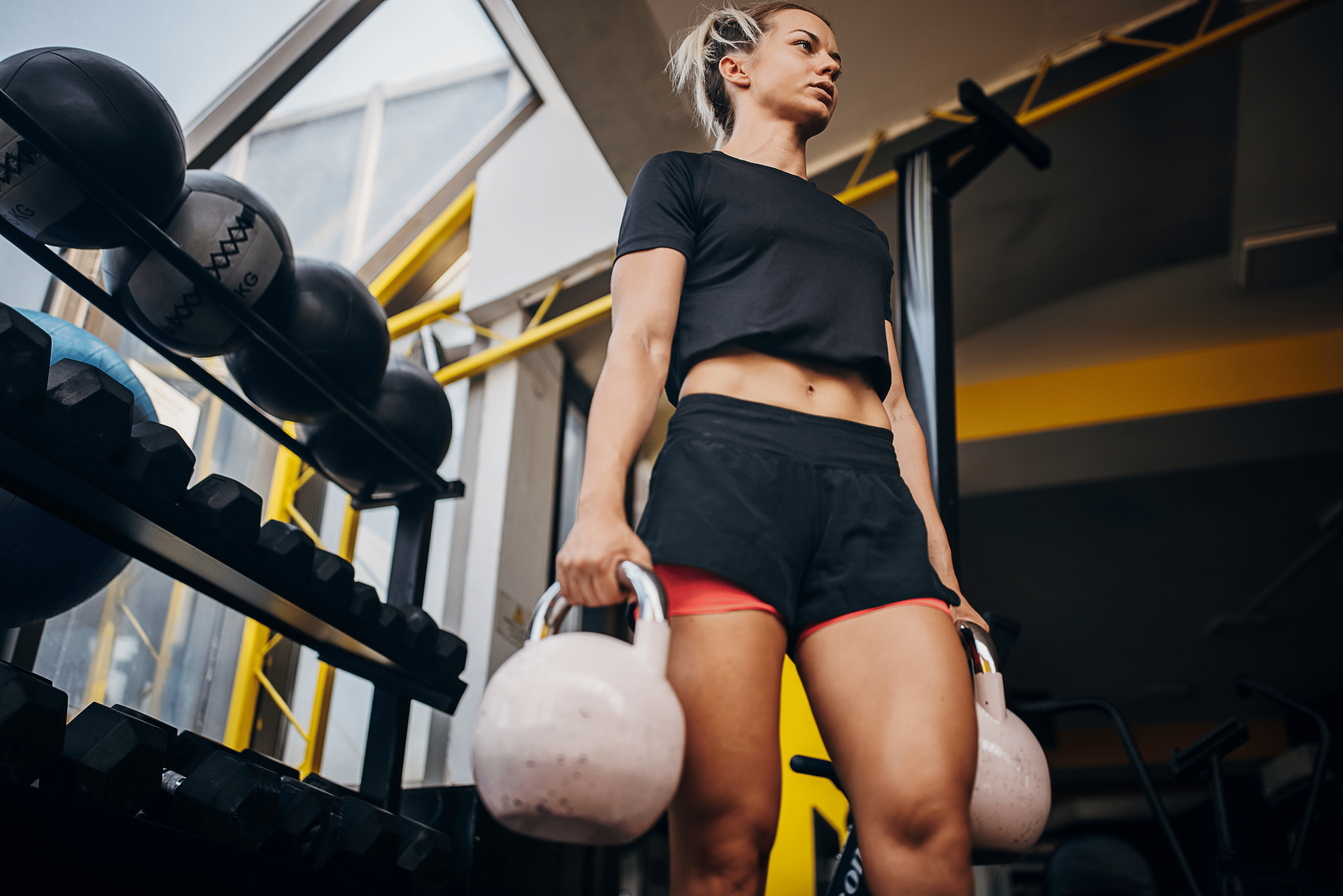 Young woman in the gym holding two kettlebells while doing a farmer's carry exercise