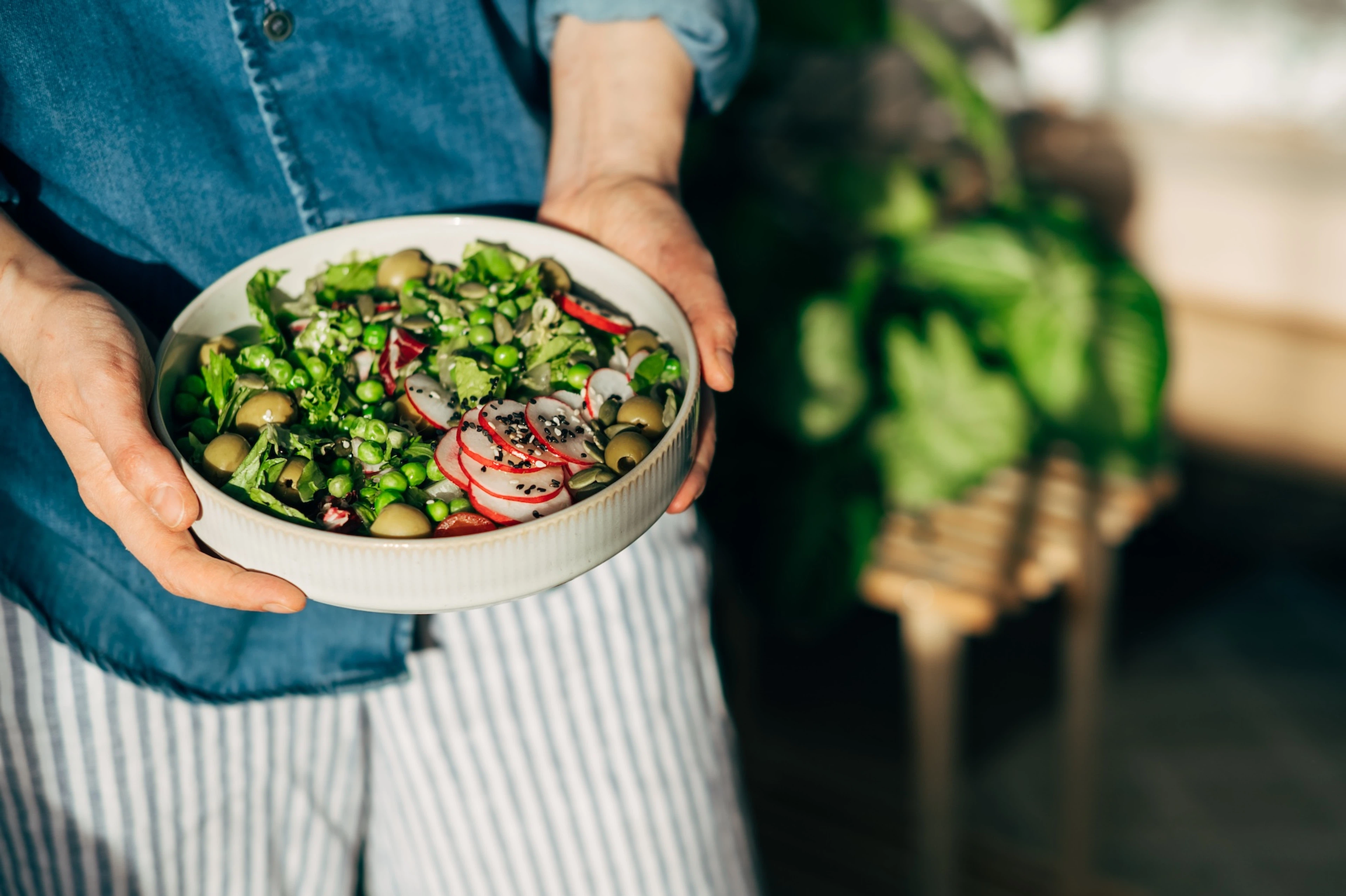 A woman carrying a plant-based salad that contains edamame, radishes, olives, greens, and more. Adding beans to salads is a good way to add more protein to your diet.