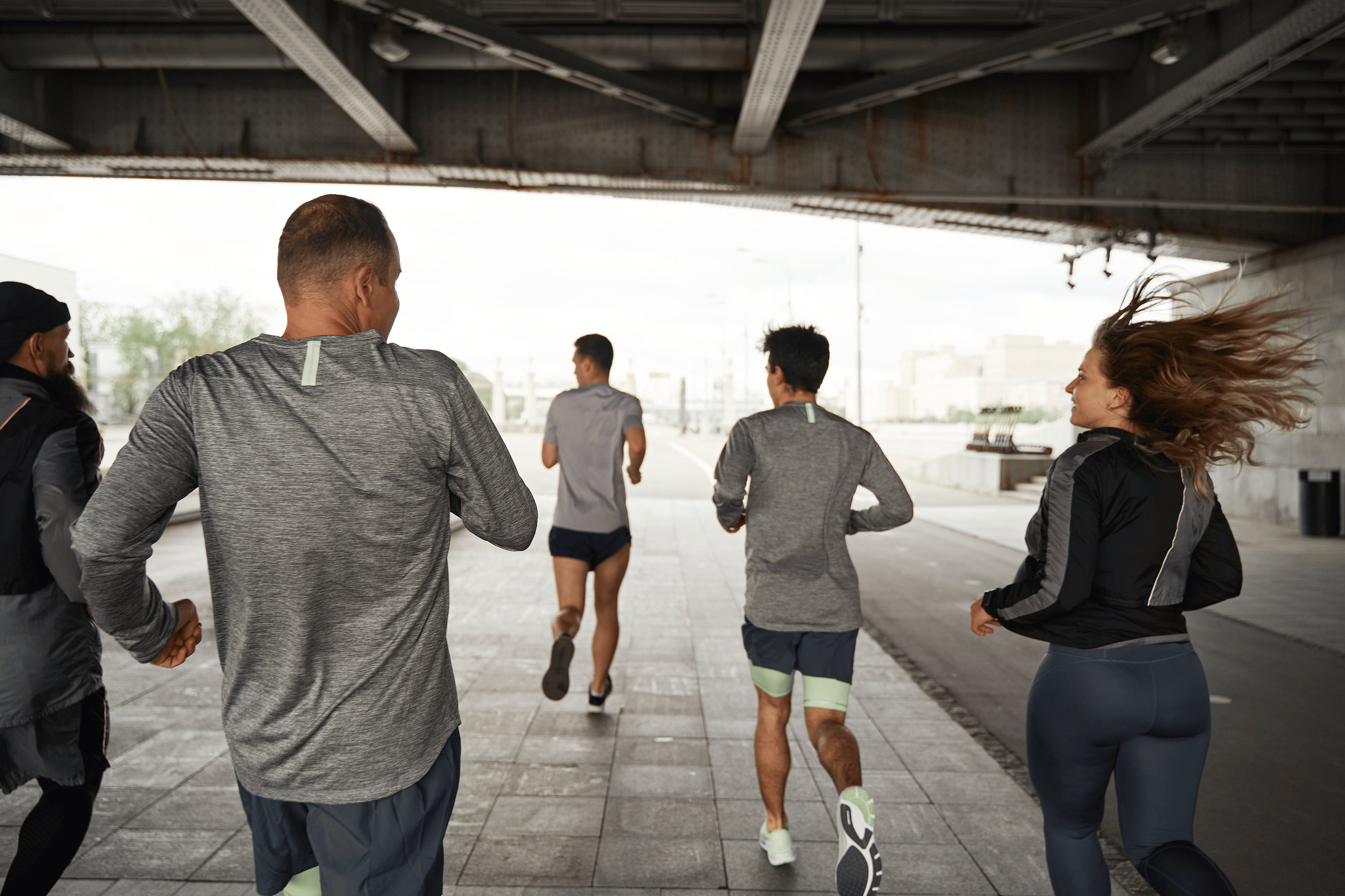 A run club jogging together under a bridge while pursuing their running goals.