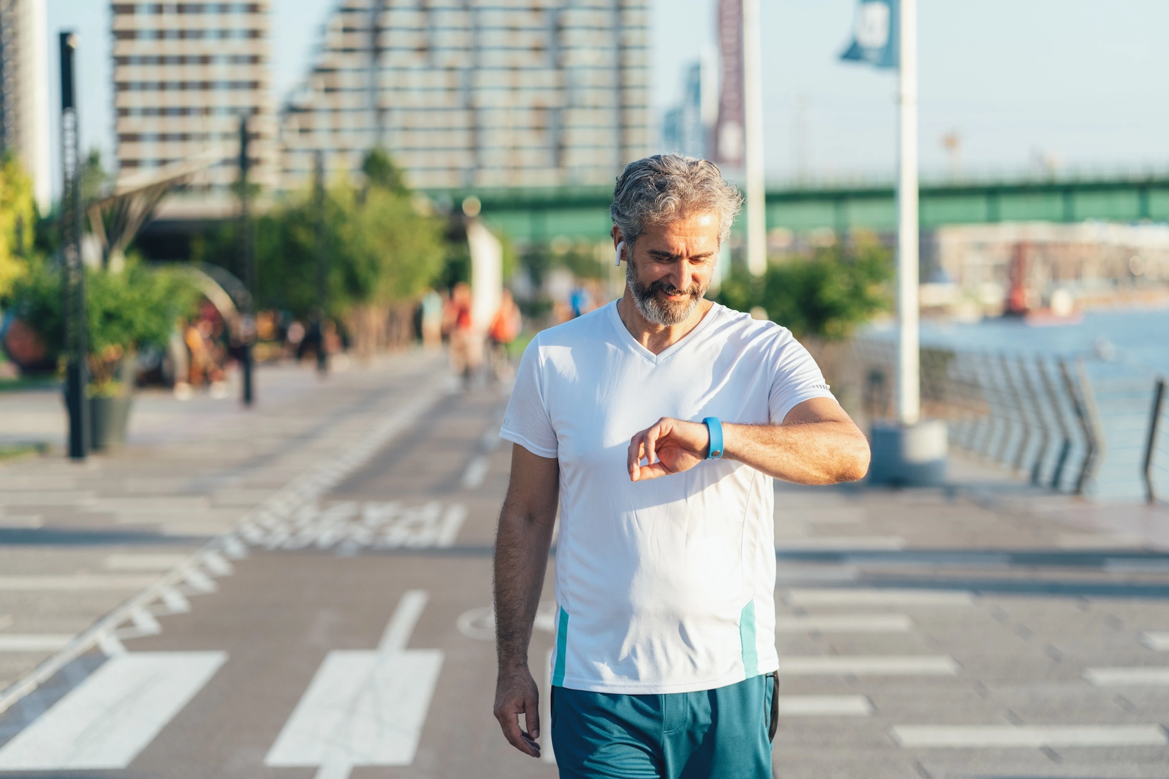 A man looking at his sports watch while walking outside for five minutes.