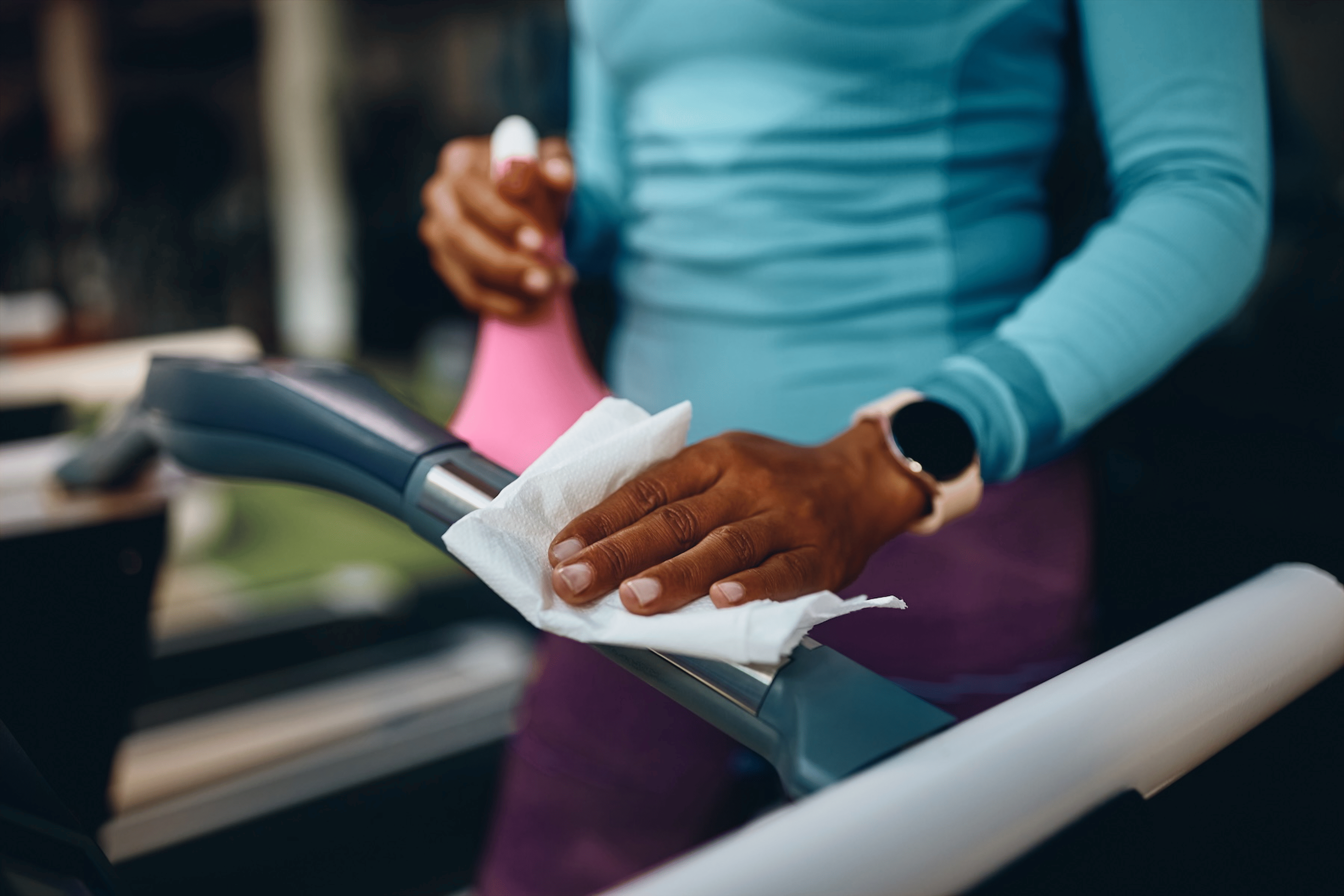 A close-up photo of a woman practicing proper gym etiquette by wiping down a cardio machine she just used.