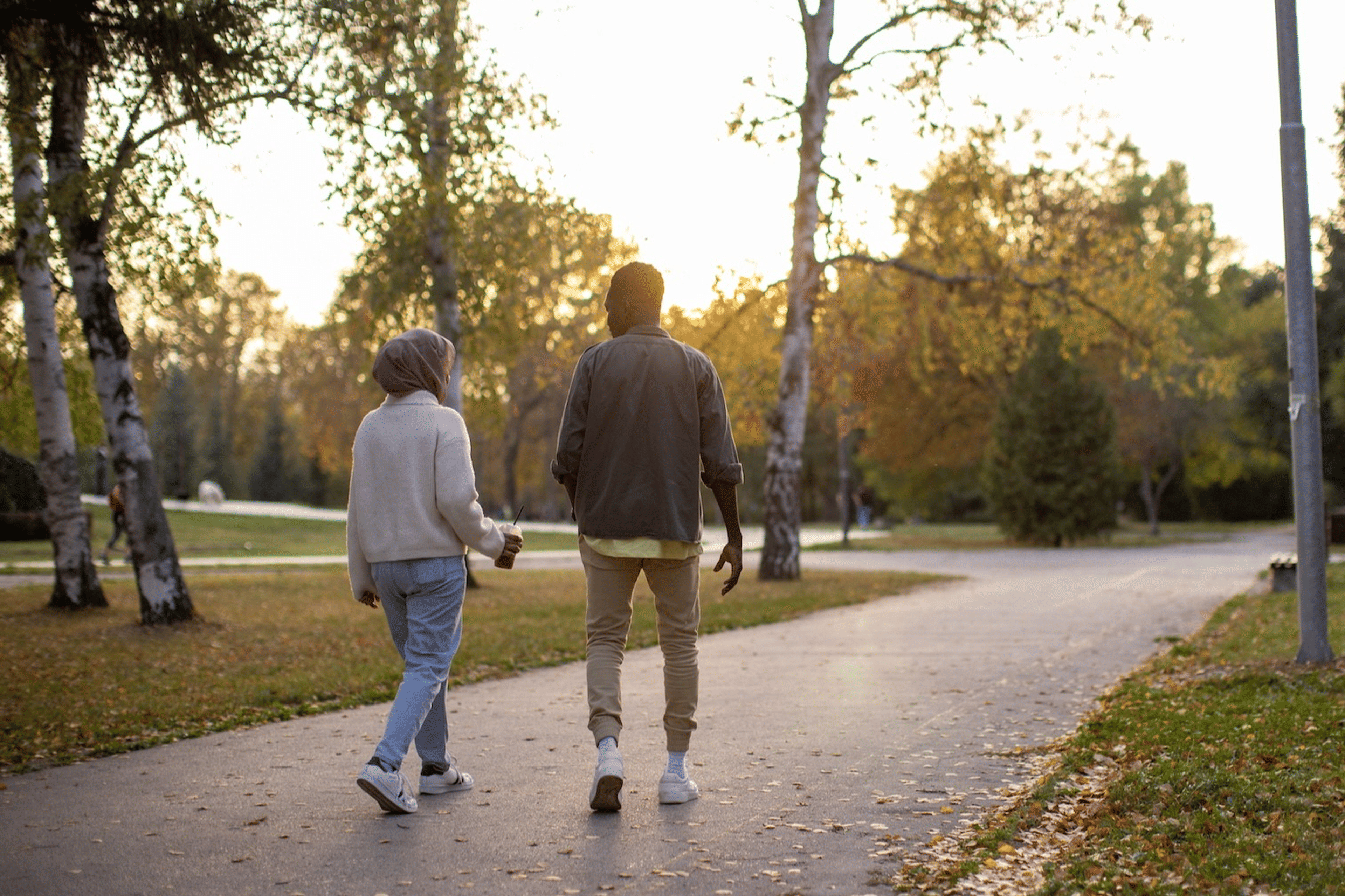 A back view of a couple going on a "fart walk" through an outdoor park on an autumn evening.