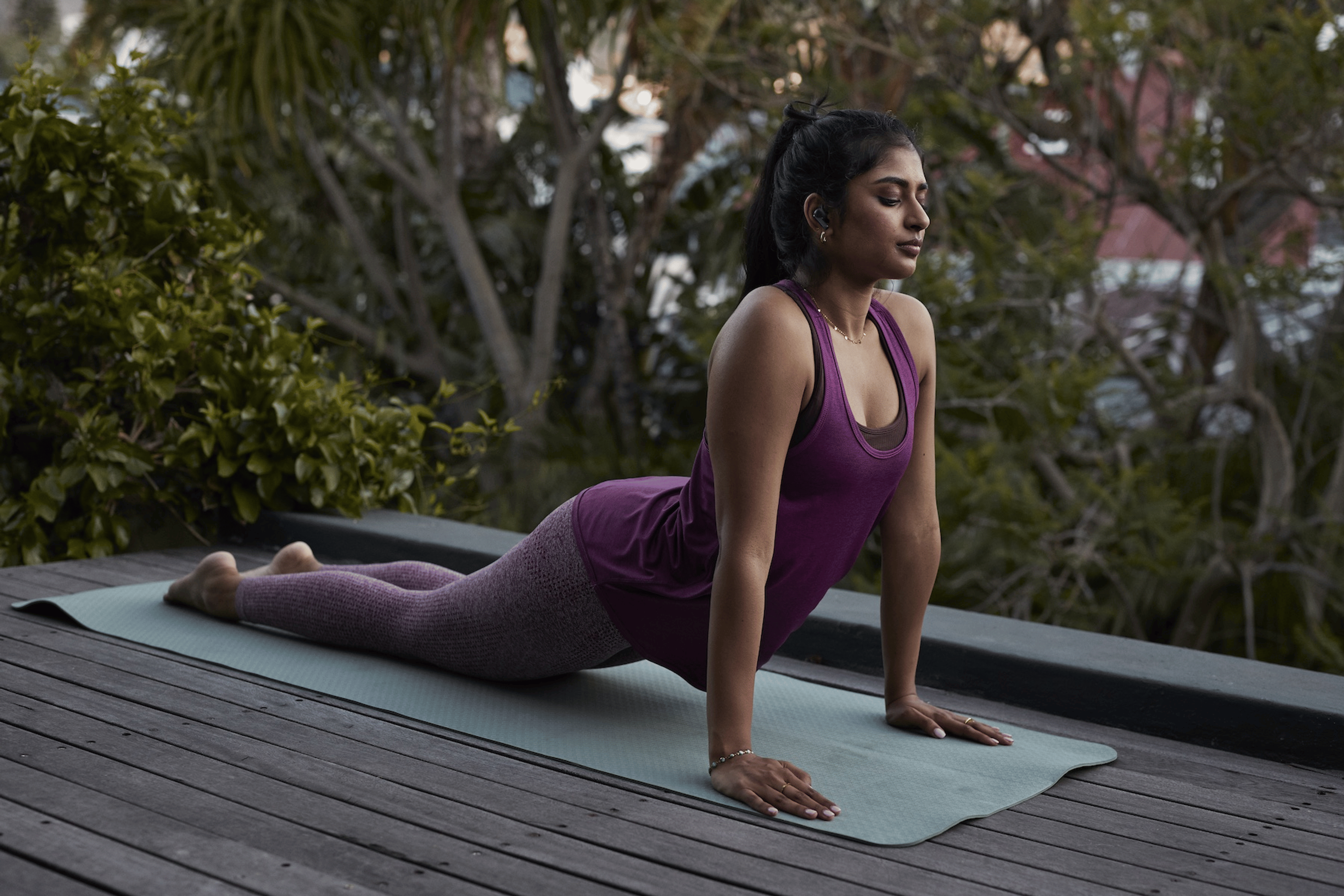 A woman practicing yoga before or after a workout. She is in Cobra Pose on a yoga mat outside on a wooden patio.