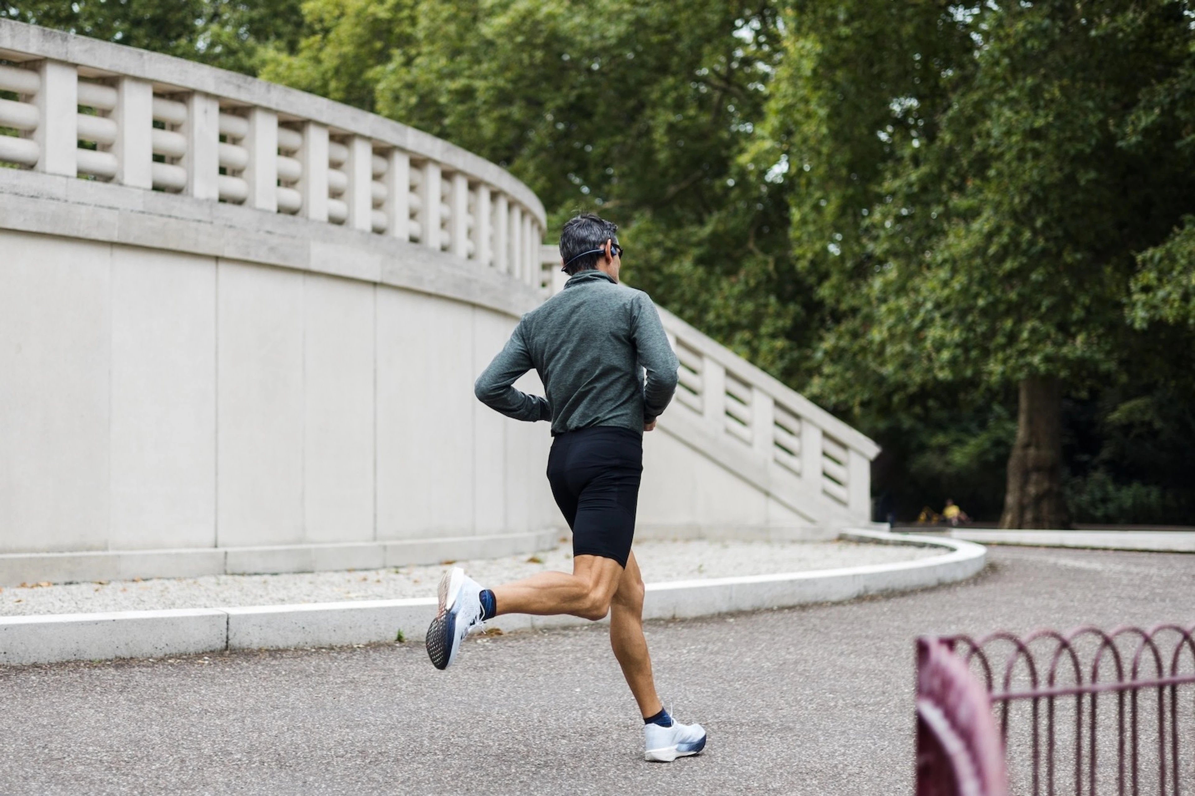A photo of a man from the back as he goes on a run outdoors. He's wearing biker shorts, a long sleeve shirt, and sunglasses.