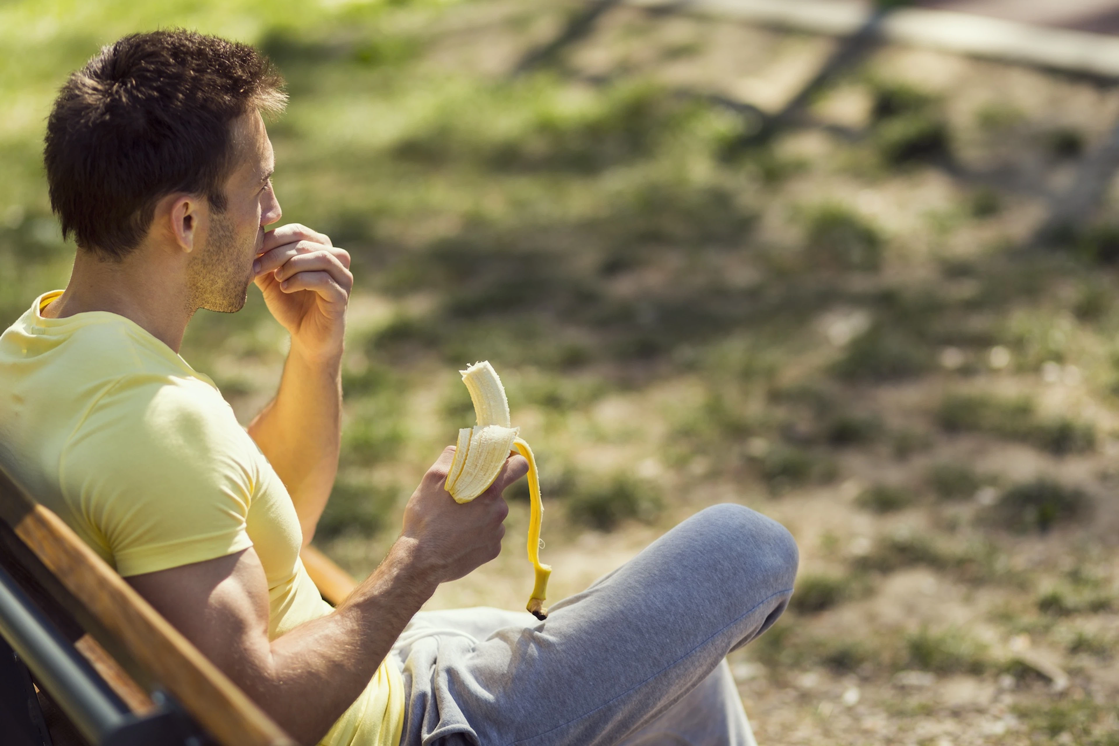 A man sitting on a park bench and eating a banana before a workout.