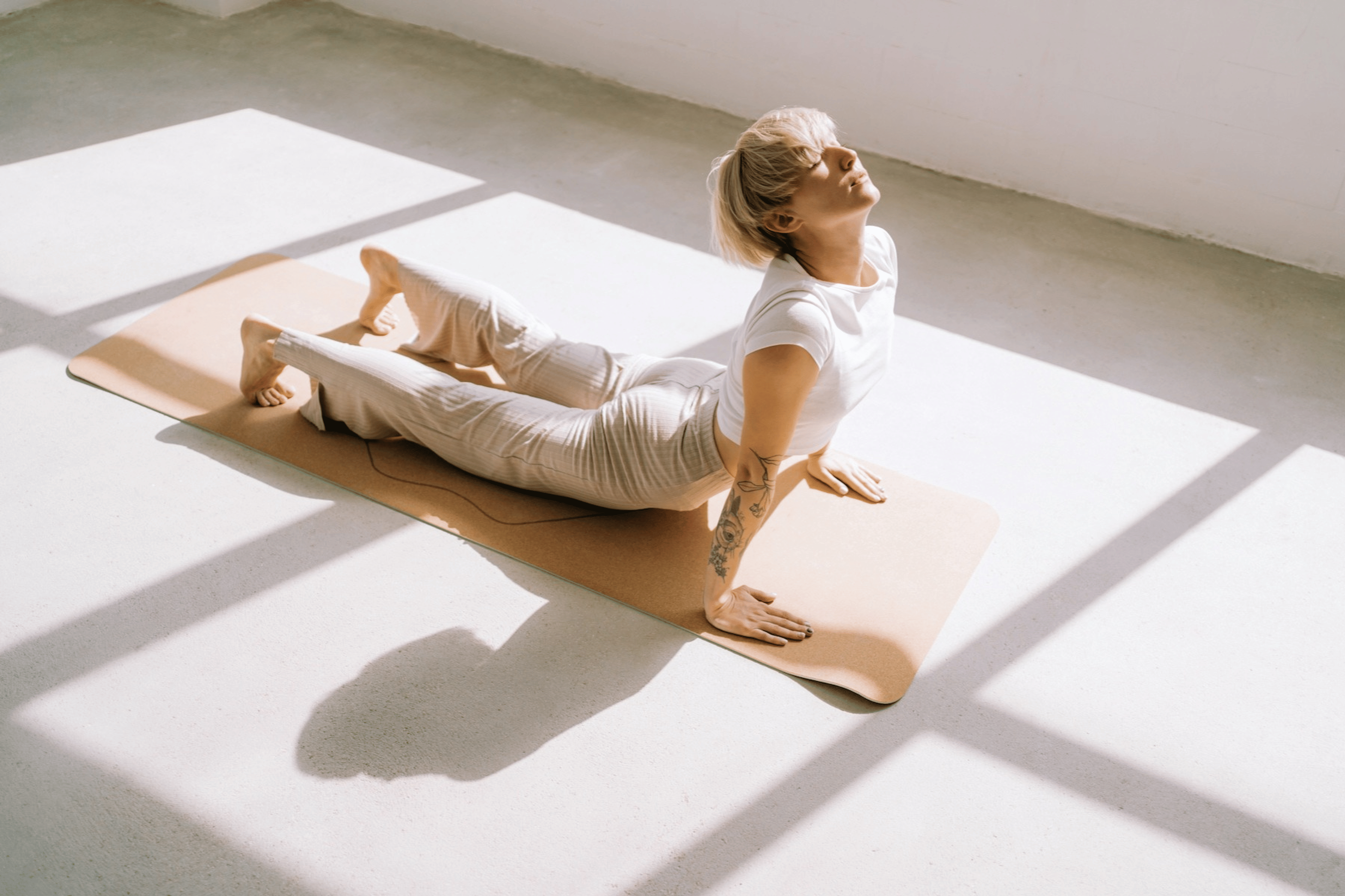 A woman practicing yoga. She's in Cobra Pose on a mat in a sunny room.
