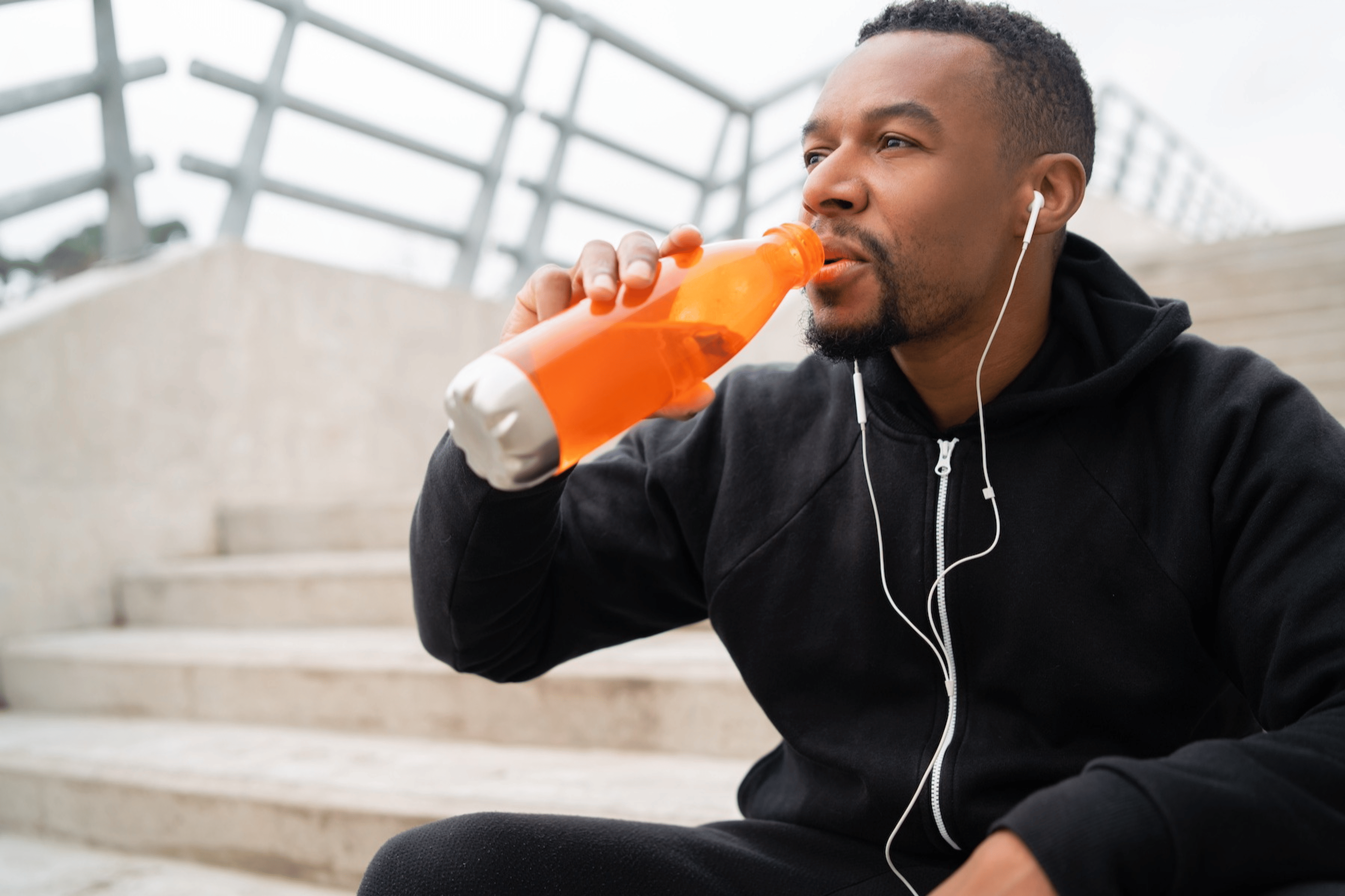 A man drinking fluids from an orange bottle after a workout.