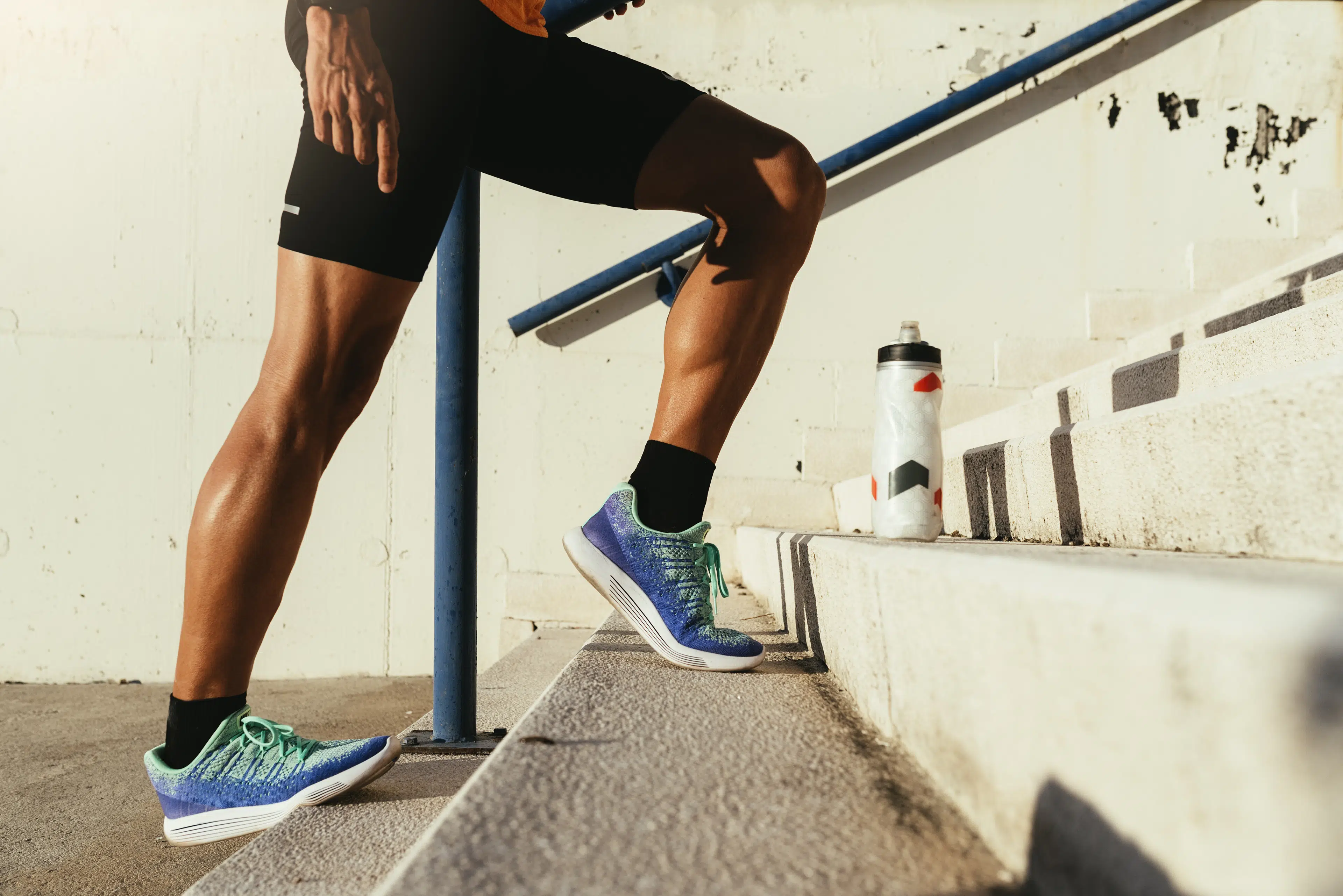 Runner standing on a staircase outside doing calf stretches and calf raises.